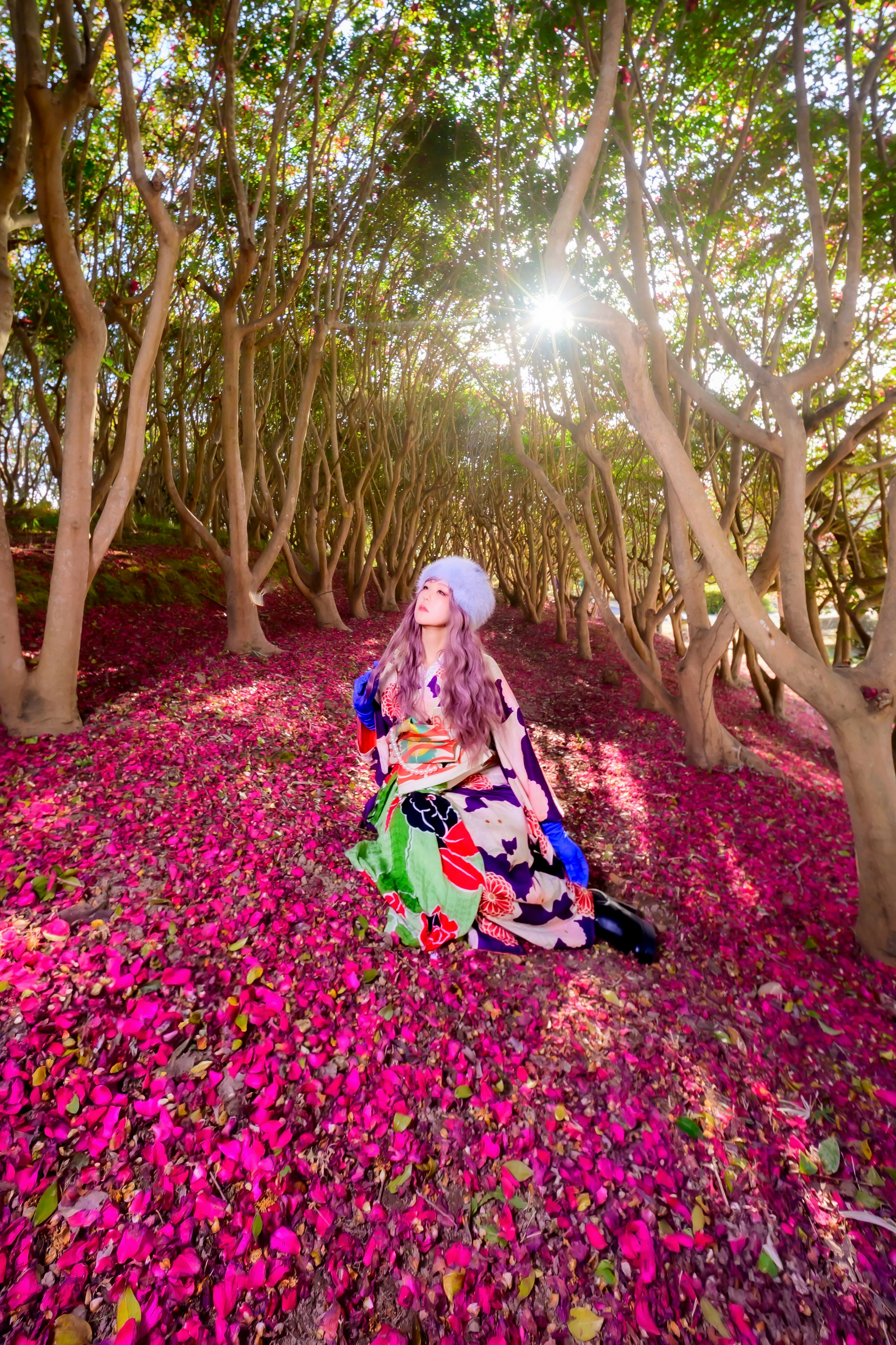 Une femme en robe colorée assise sur un tapis de pétales de fleurs dans une forêt