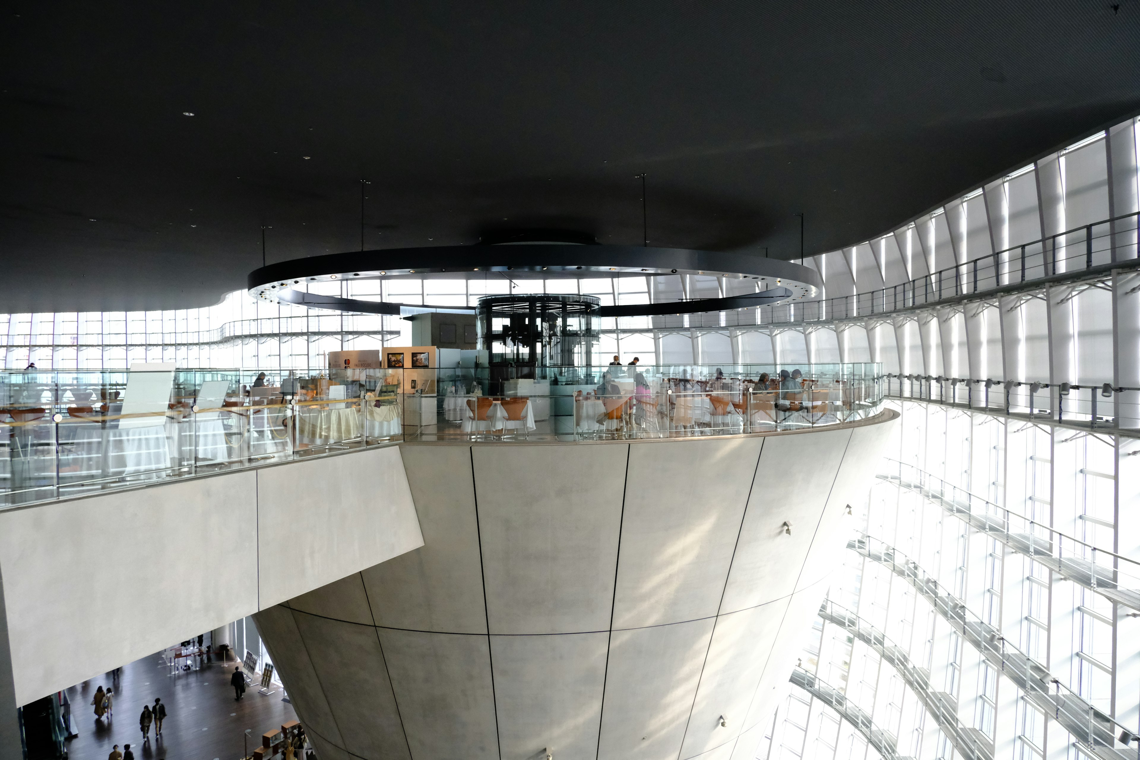 Interior view of modern architectural design featuring large glass windows allowing natural light Various people gathered in the space