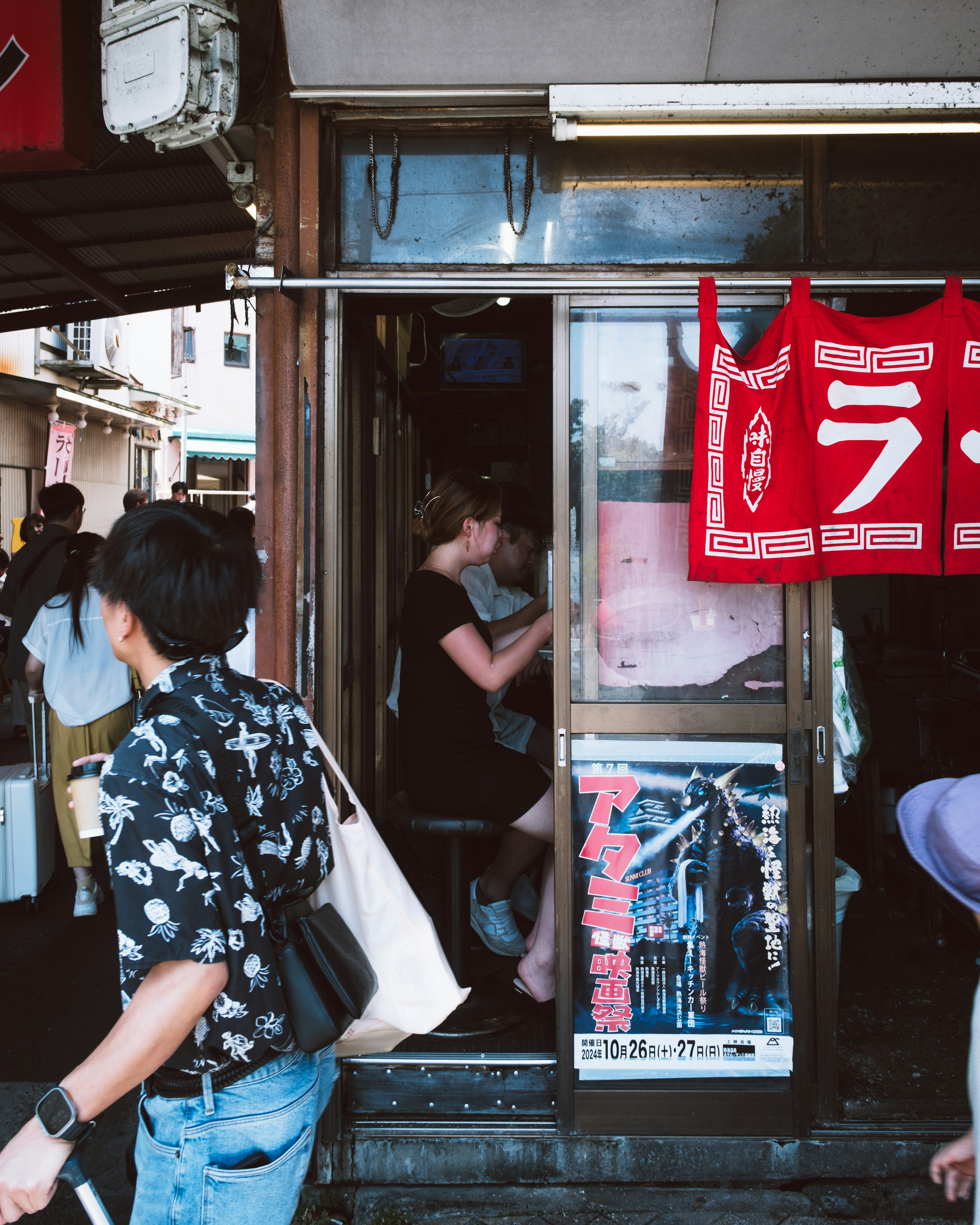 People walking by the entrance of a small shop on a busy street