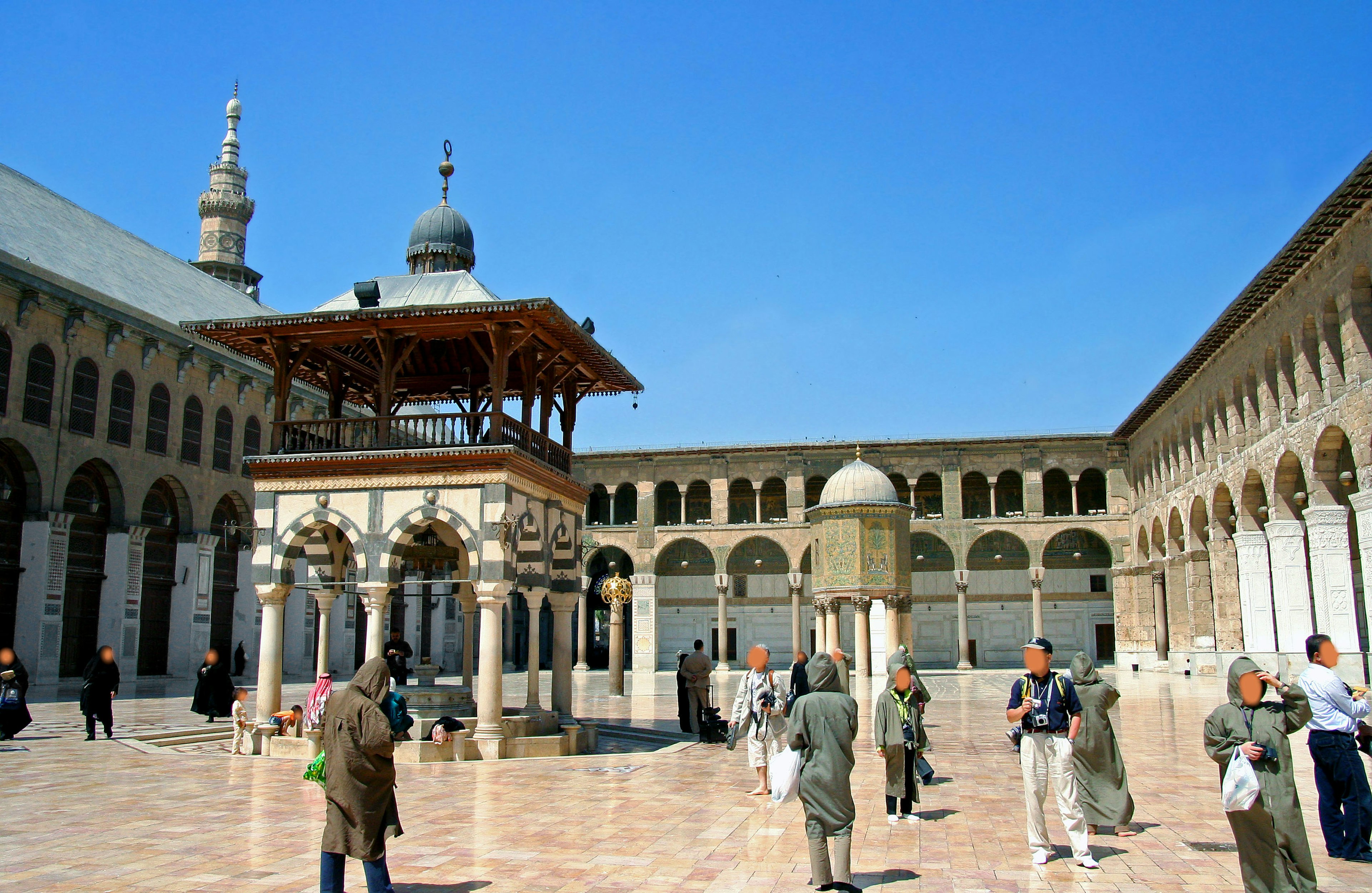 Courtyard of a mosque with people gathered under a clear blue sky