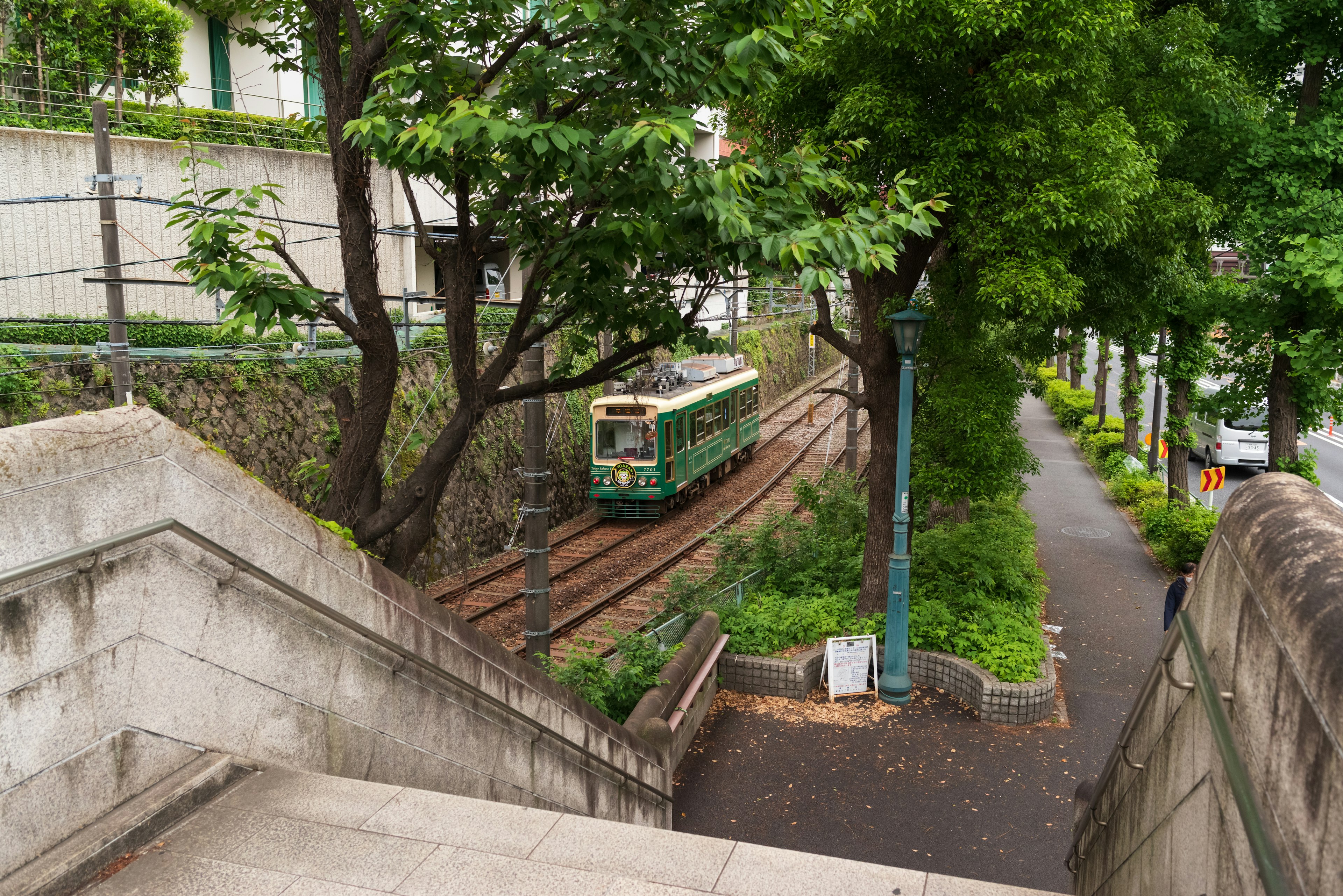 Tramway vert passant dans une zone urbaine pittoresque entourée d'arbres et d'escaliers