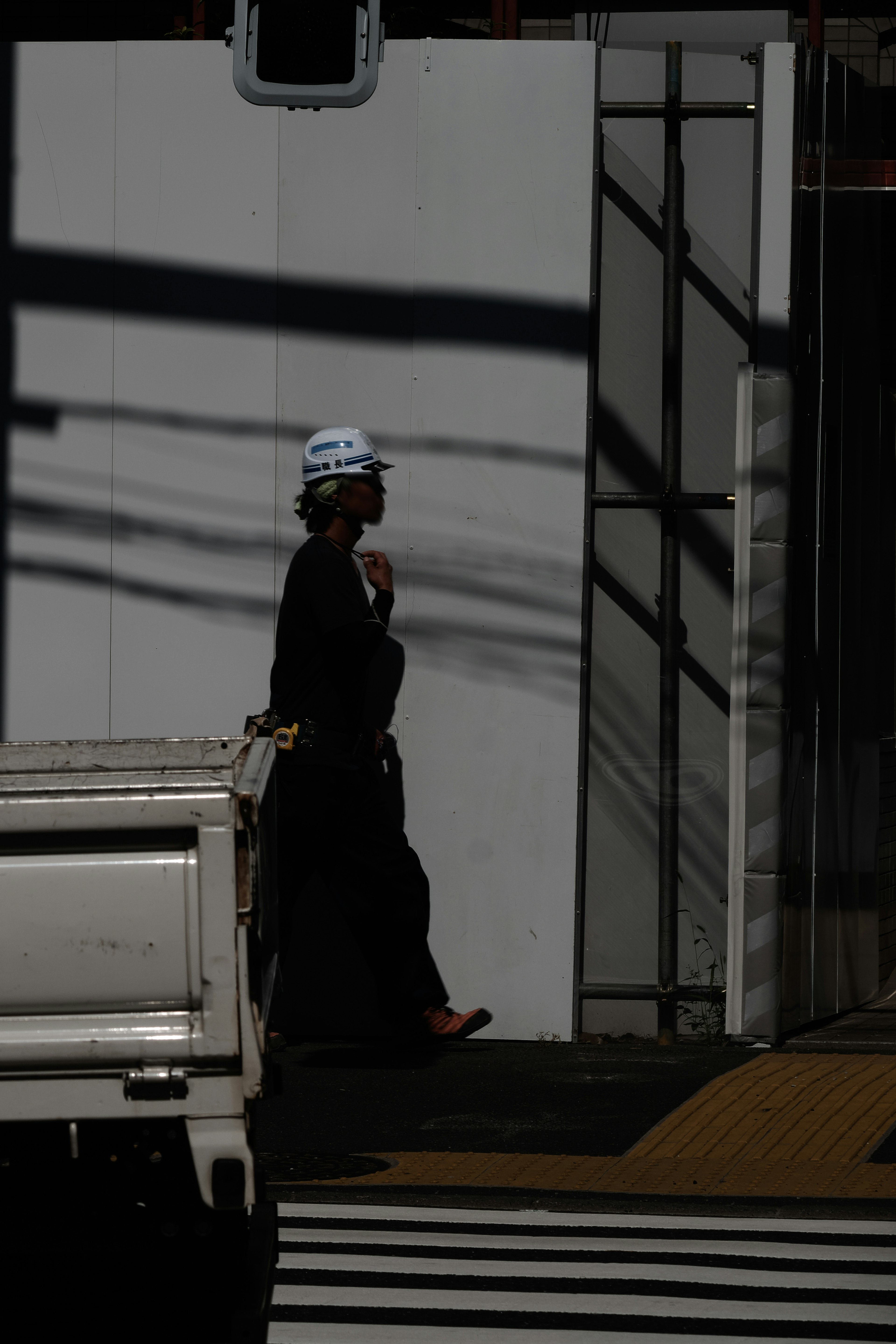 Una figura caminando en sombras contra una pared blanca