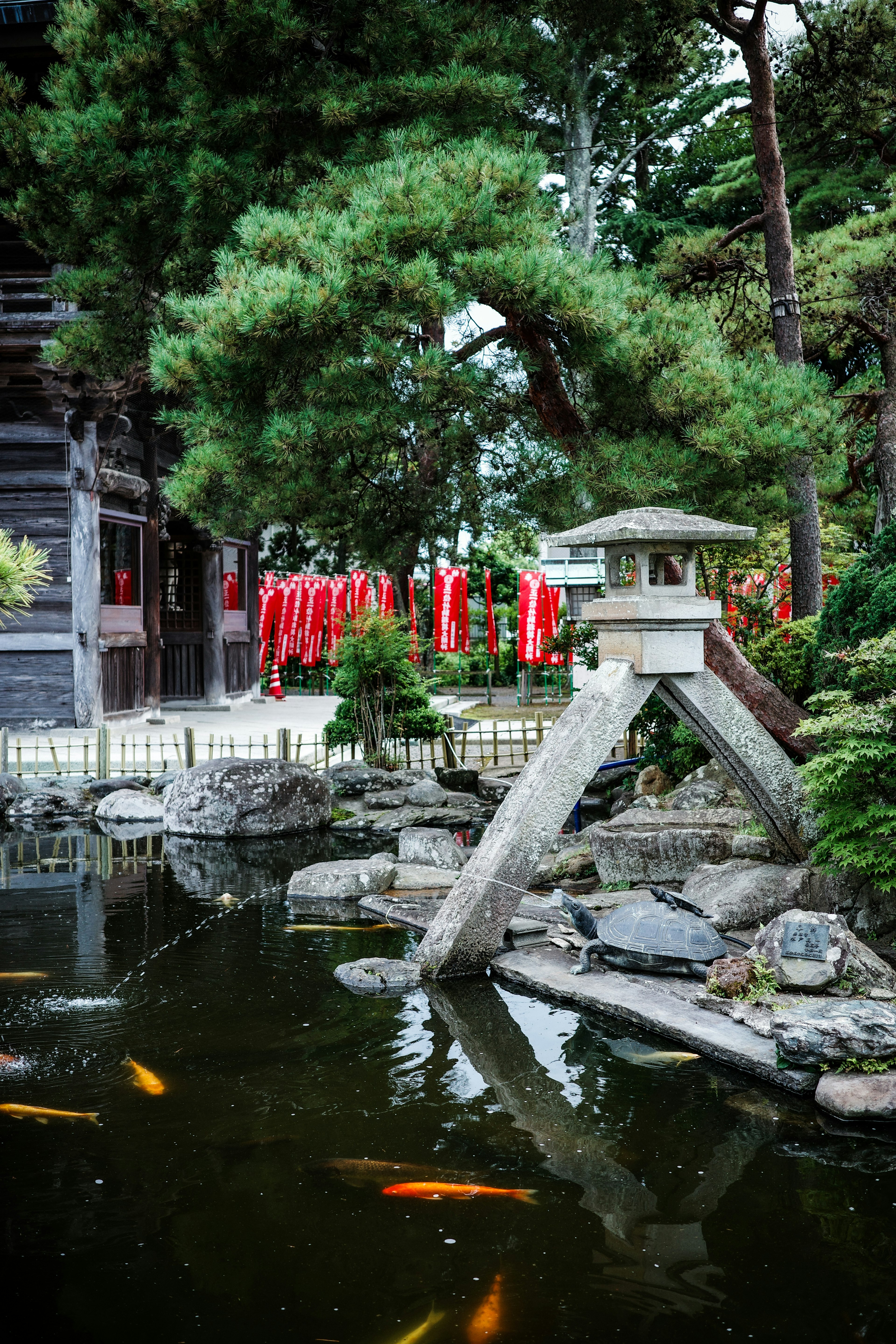 池のそばにある石の灯籠と金魚が泳ぐ風景