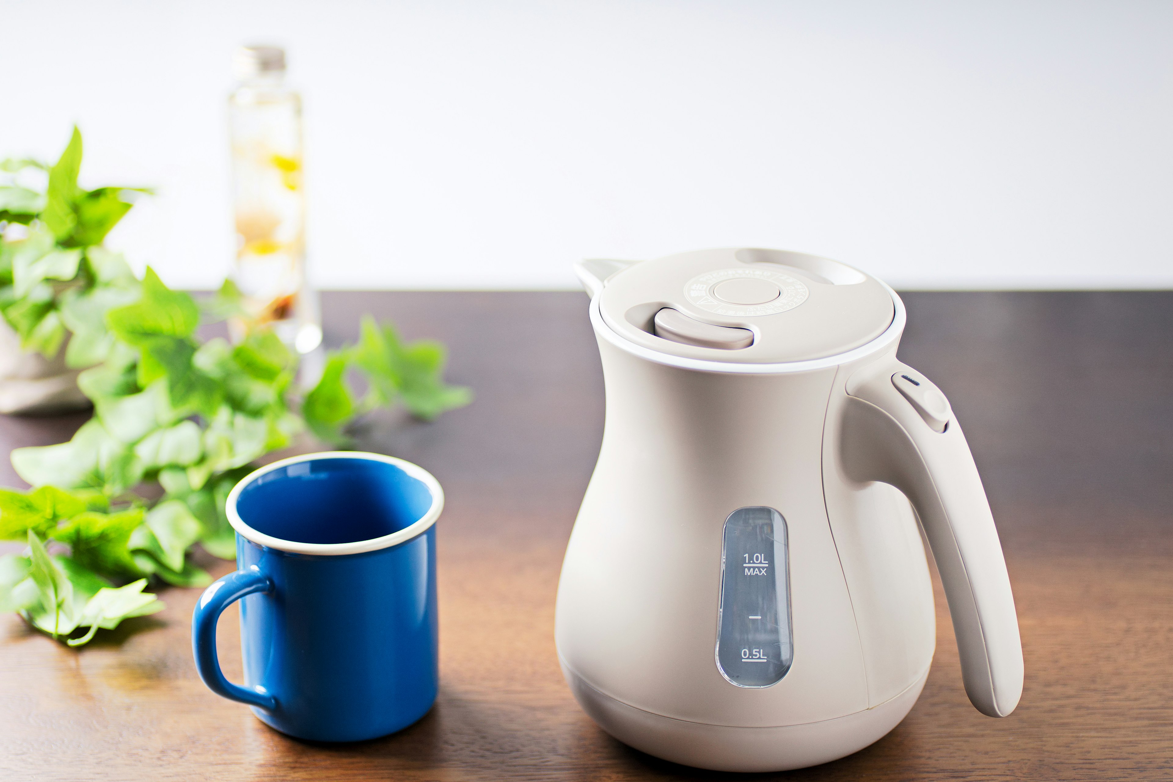 Una tetera eléctrica blanca junto a una taza azul sobre una mesa de madera