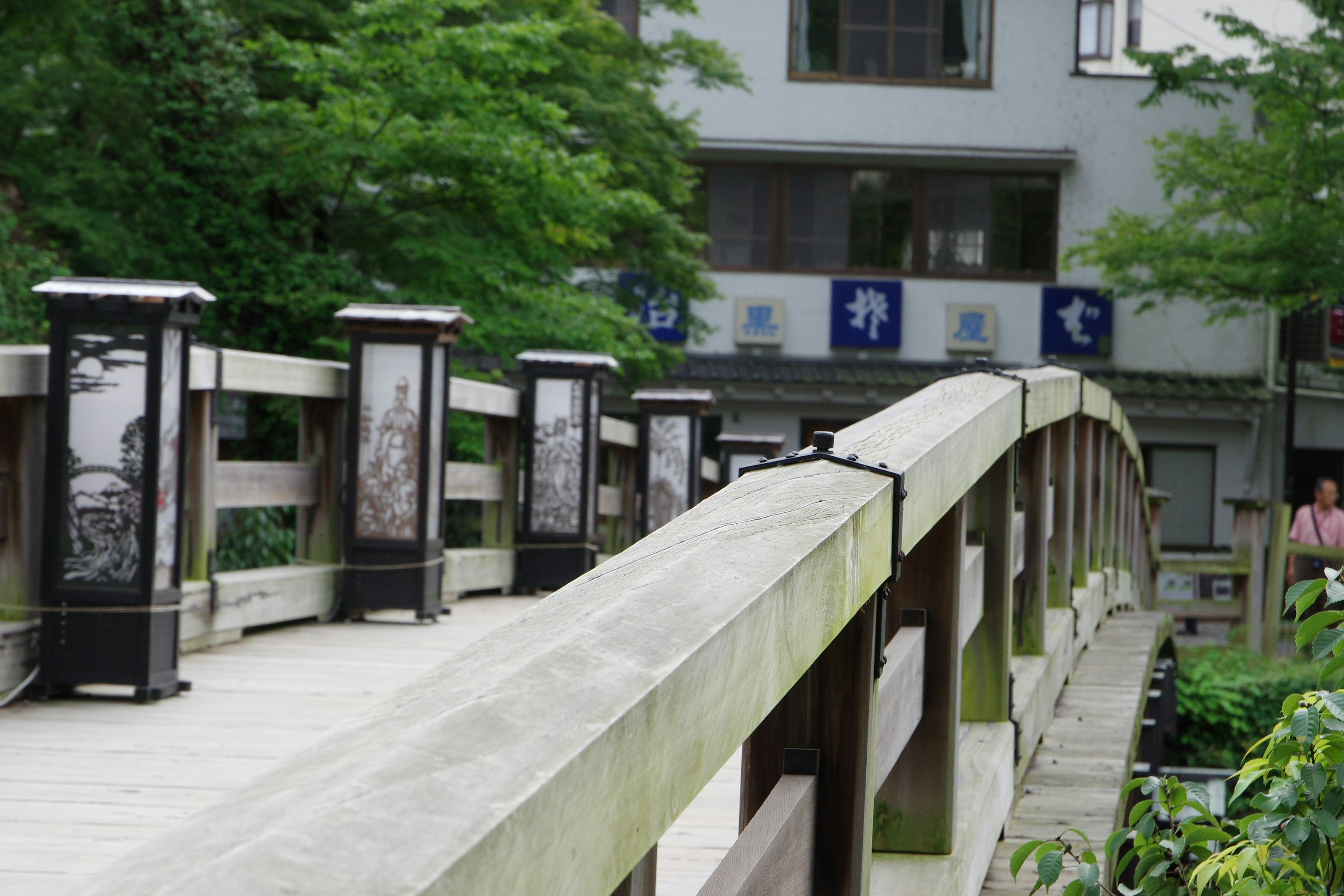 A wooden bridge surrounded by greenery with lanterns lining the sides