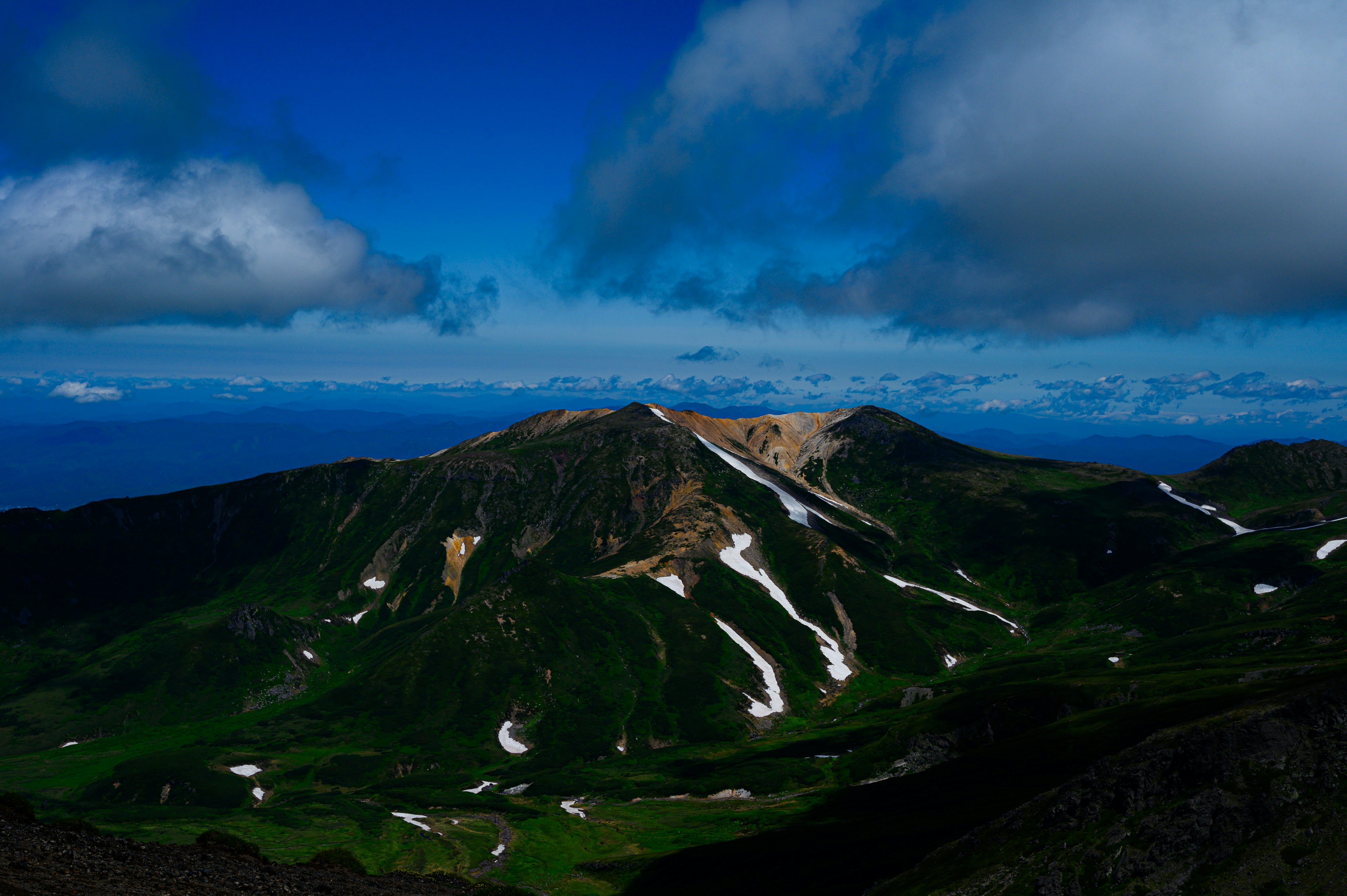 青空と雲に囲まれた緑豊かな山の風景 雪解けの跡が見える山頂