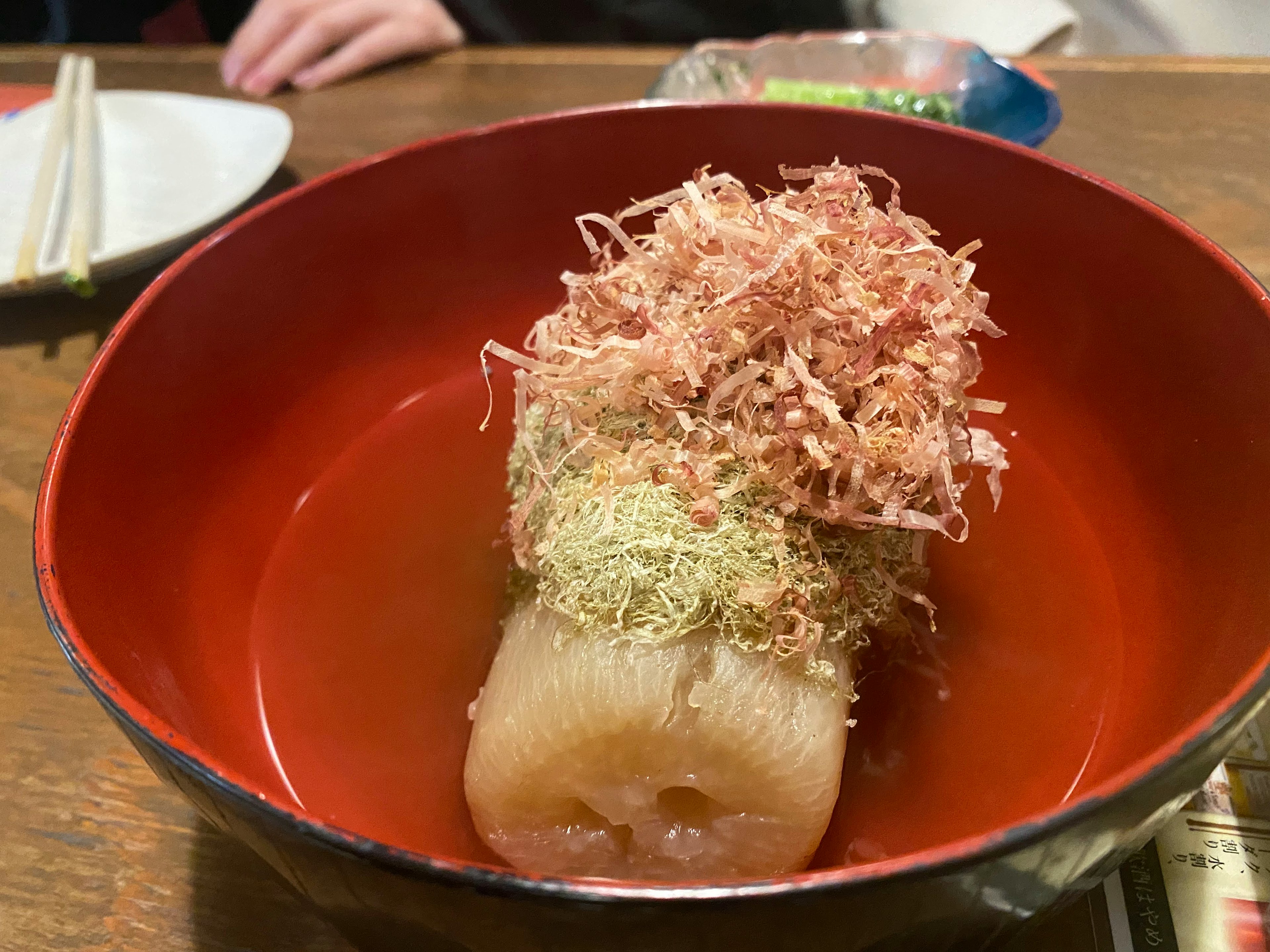 Japanisches Gericht mit Daikon, garniert mit Bonitoflocken und Aonori in einer roten Schüssel