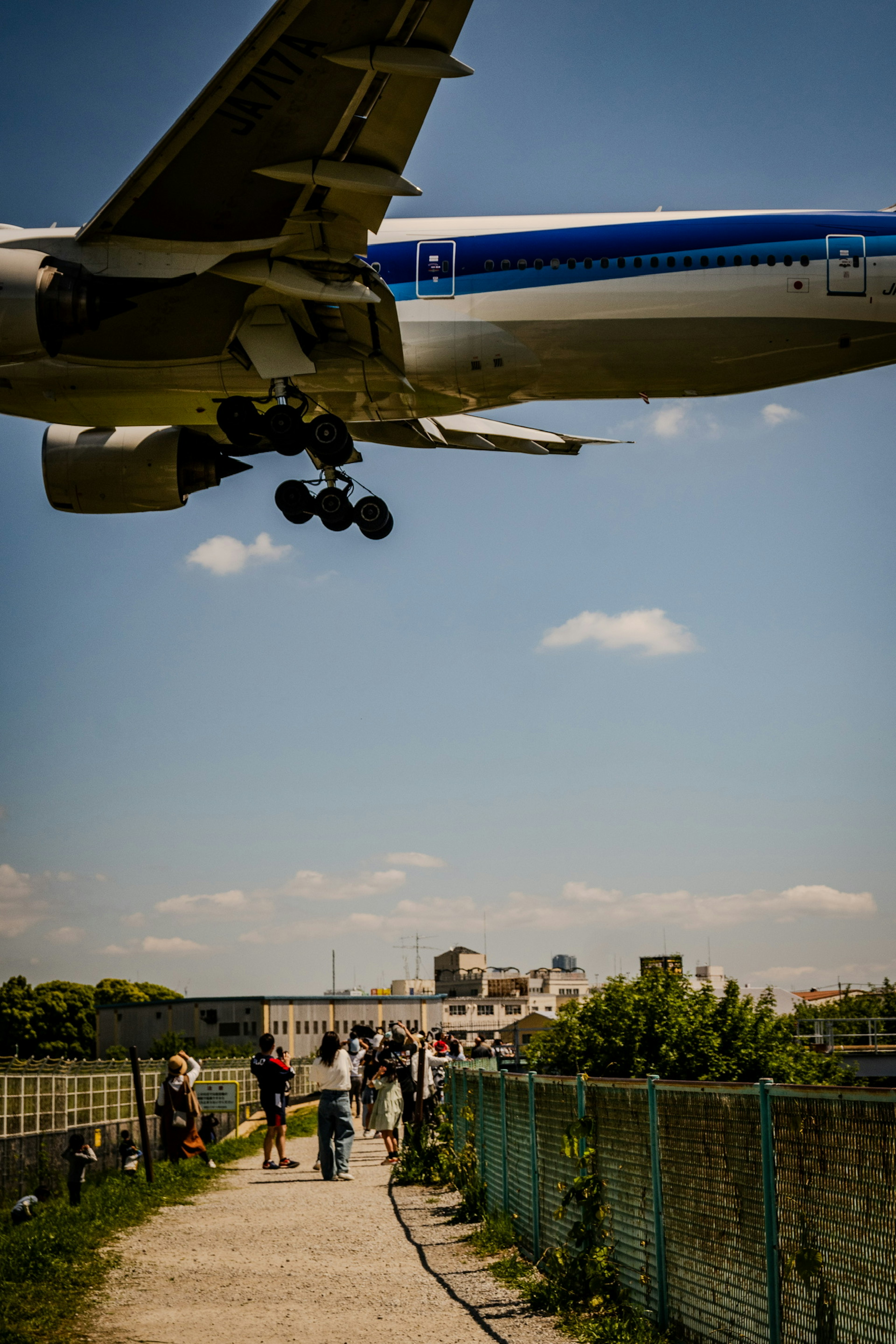 An airplane flying low against a blue sky with people walking nearby