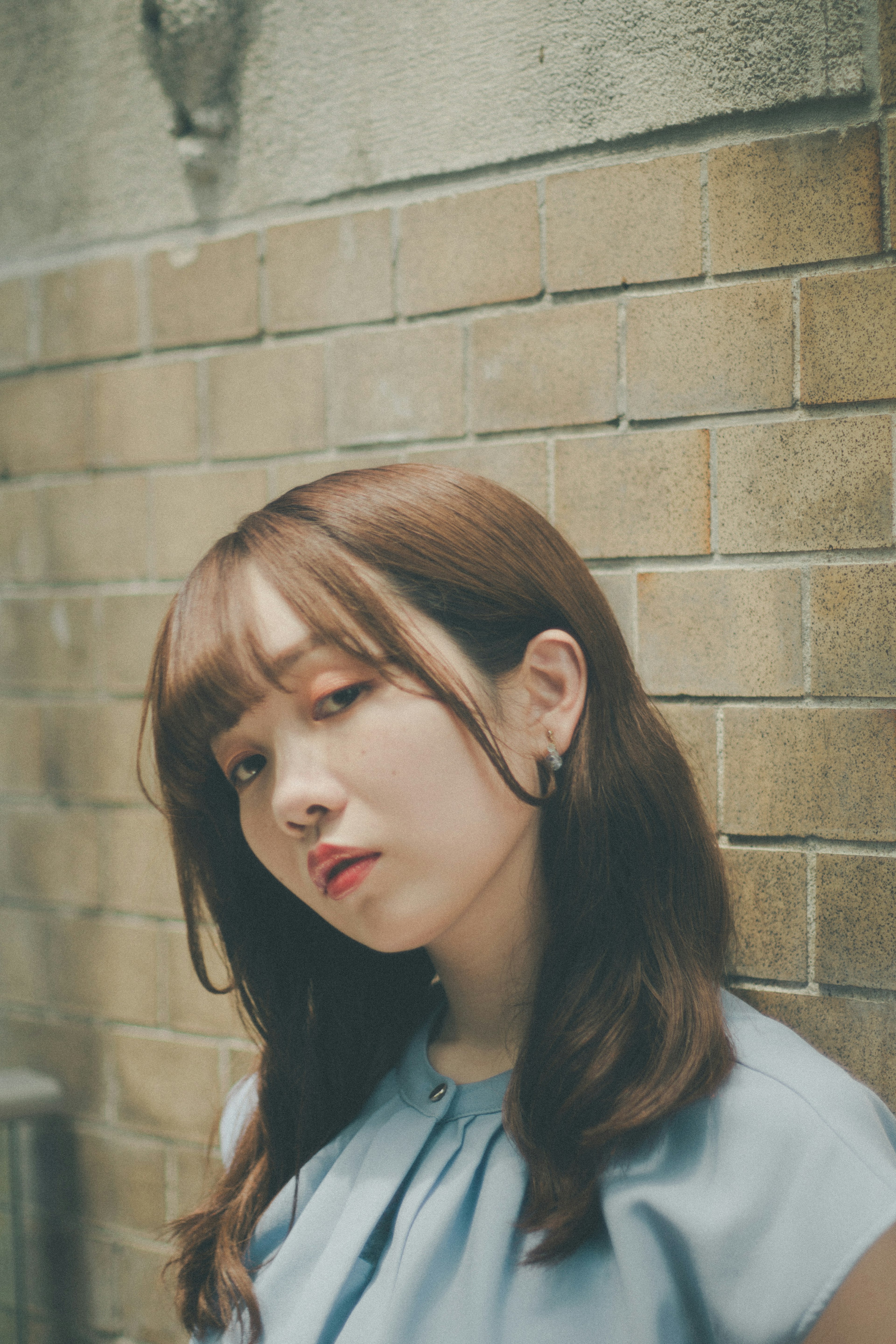 Young woman posing in front of a brick wall wearing a blue top