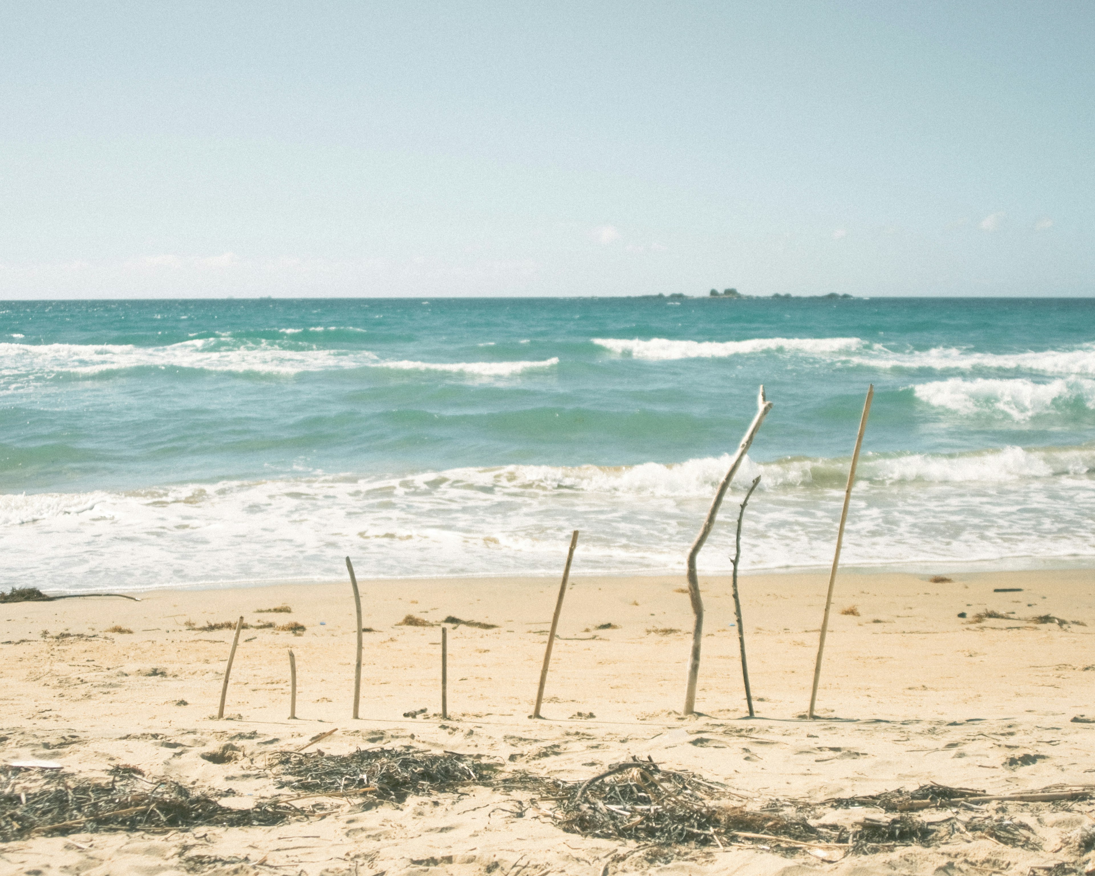 Sottili bastoni di legno in piedi sulla spiaggia sabbiosa con onde oceaniche