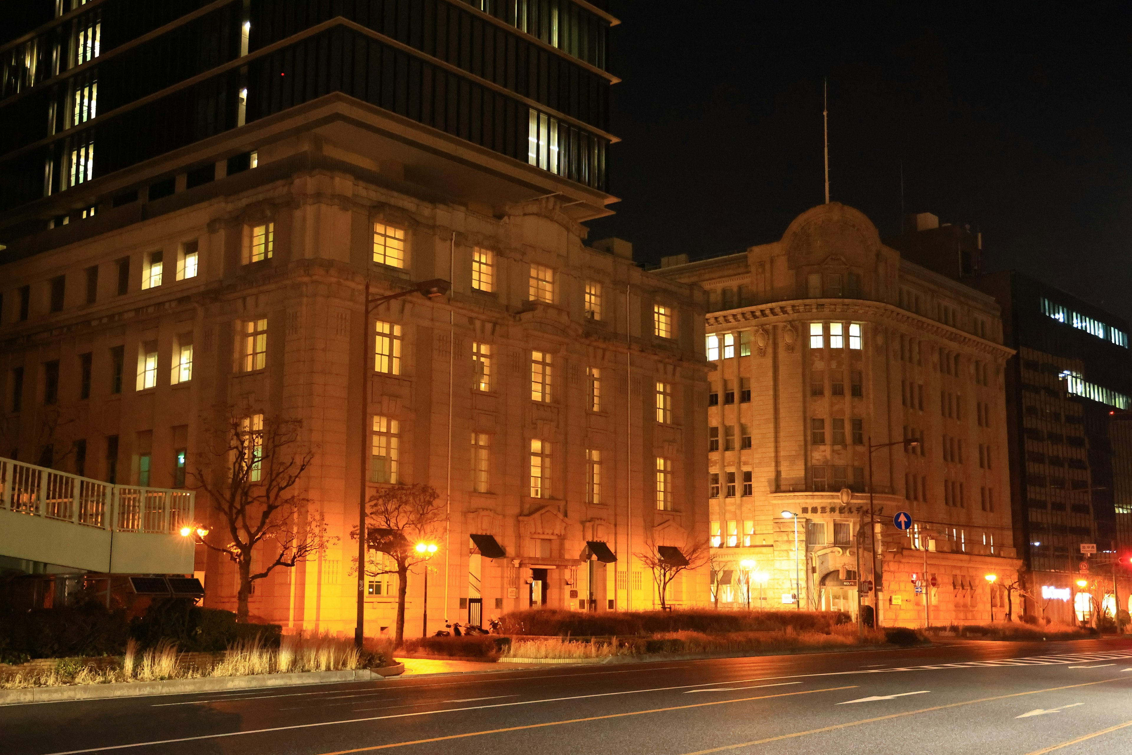 Fachada de un edificio histórico iluminada por la noche con rascacielos modernos