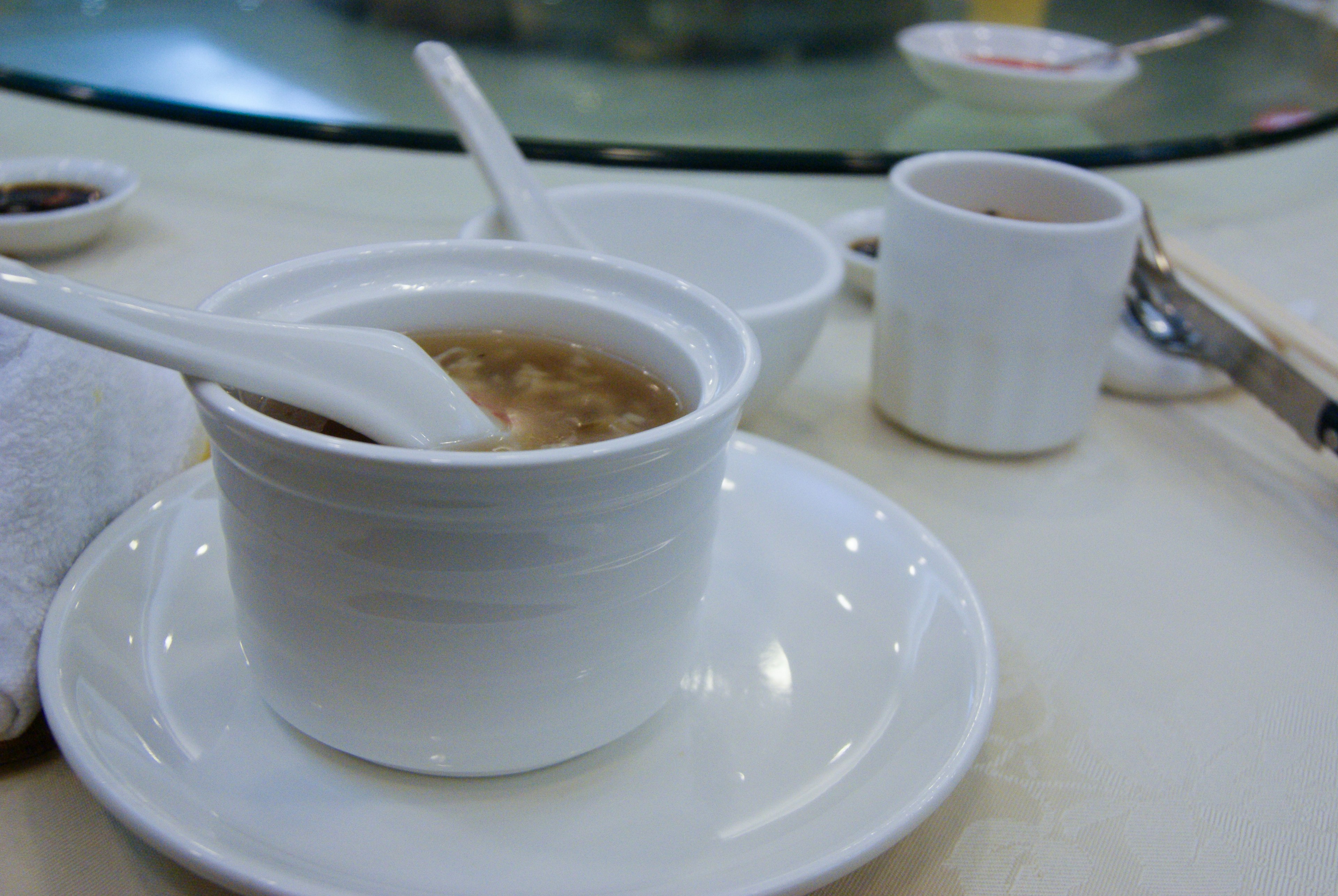 A white bowl of soup with a spoon and a small cup on a table