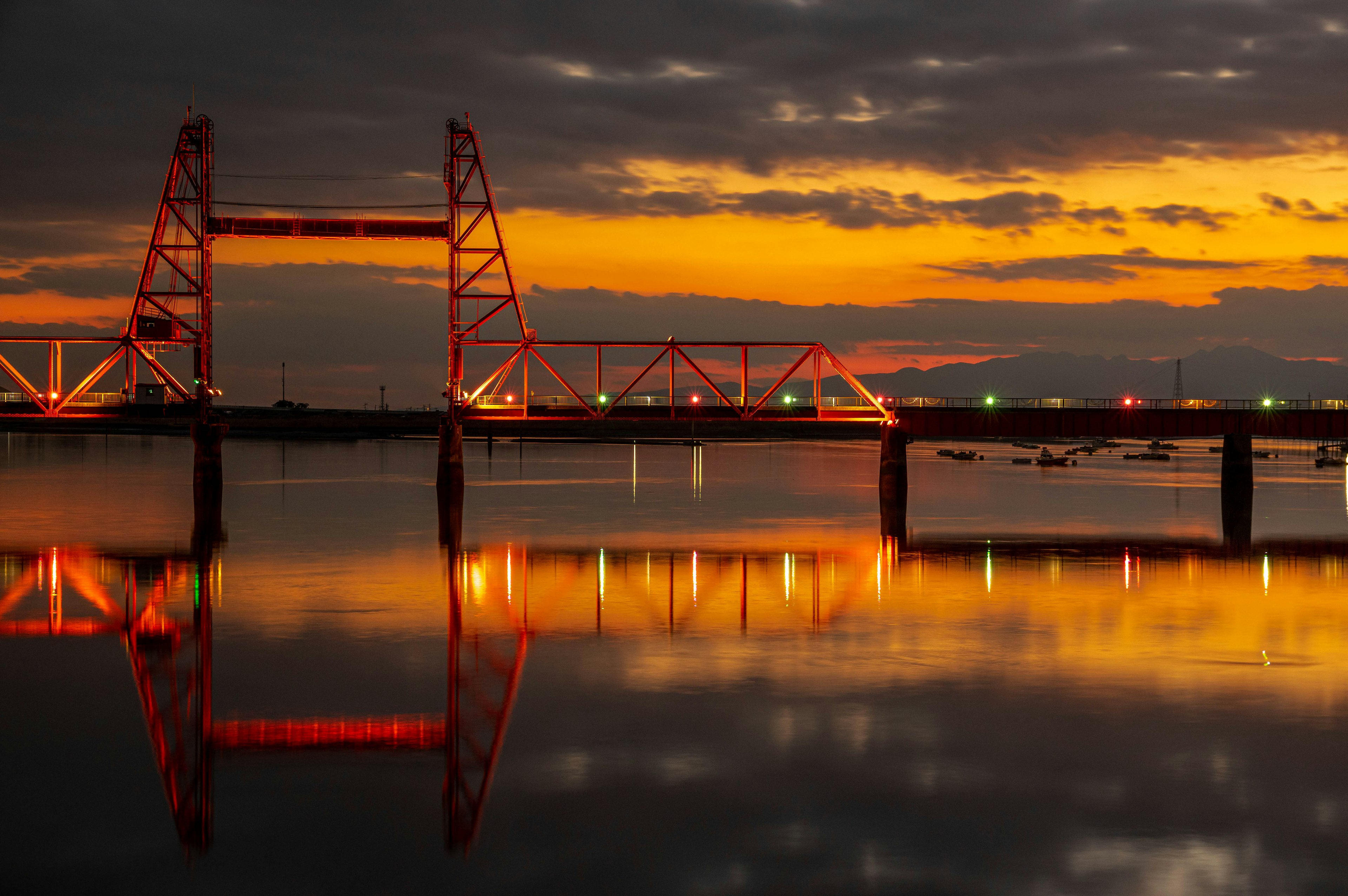 Silhouette di un ponte rosso contro un tramonto con riflessi sull'acqua