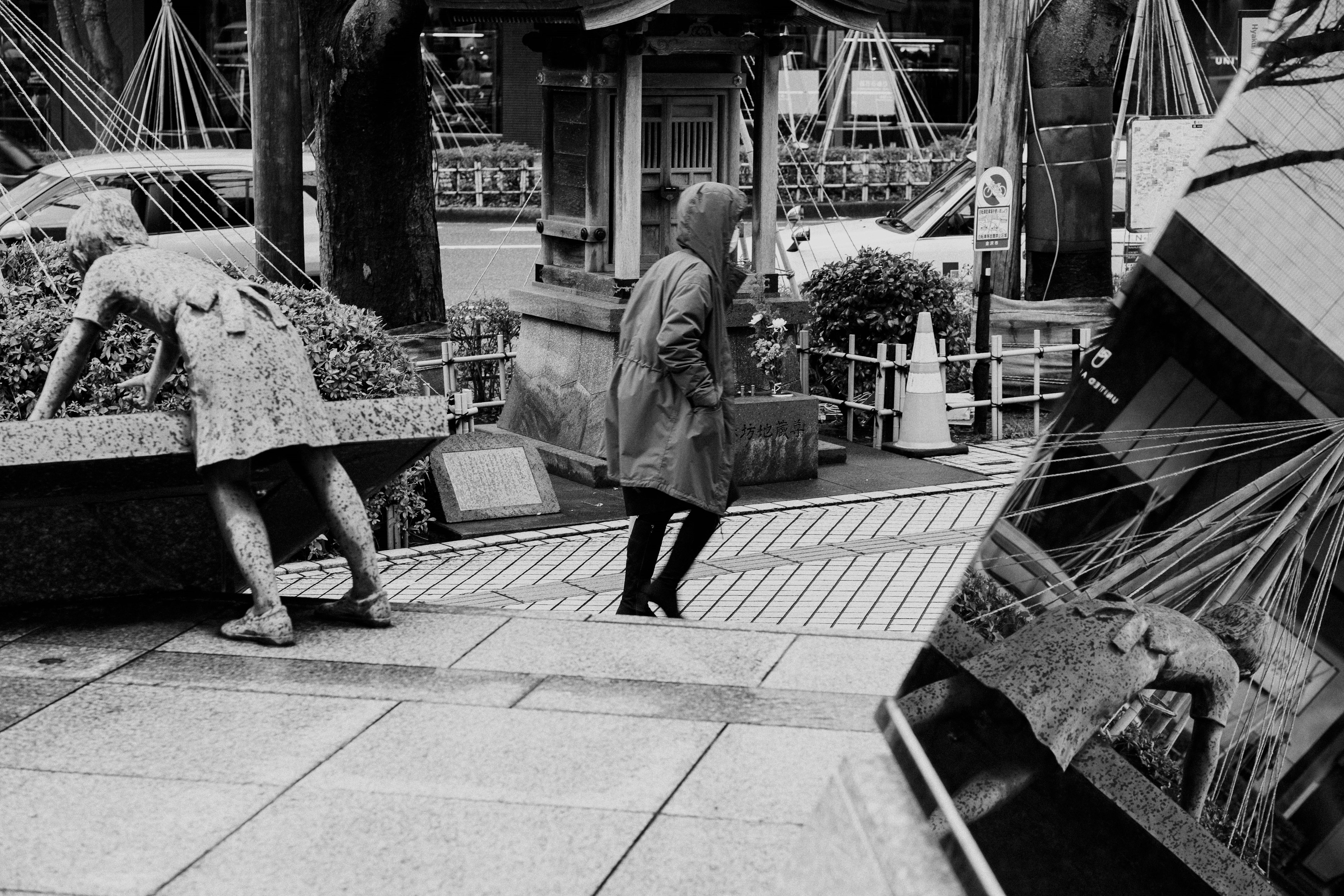 Una escena en blanco y negro con una mujer caminando y una figura parecida a una escultura