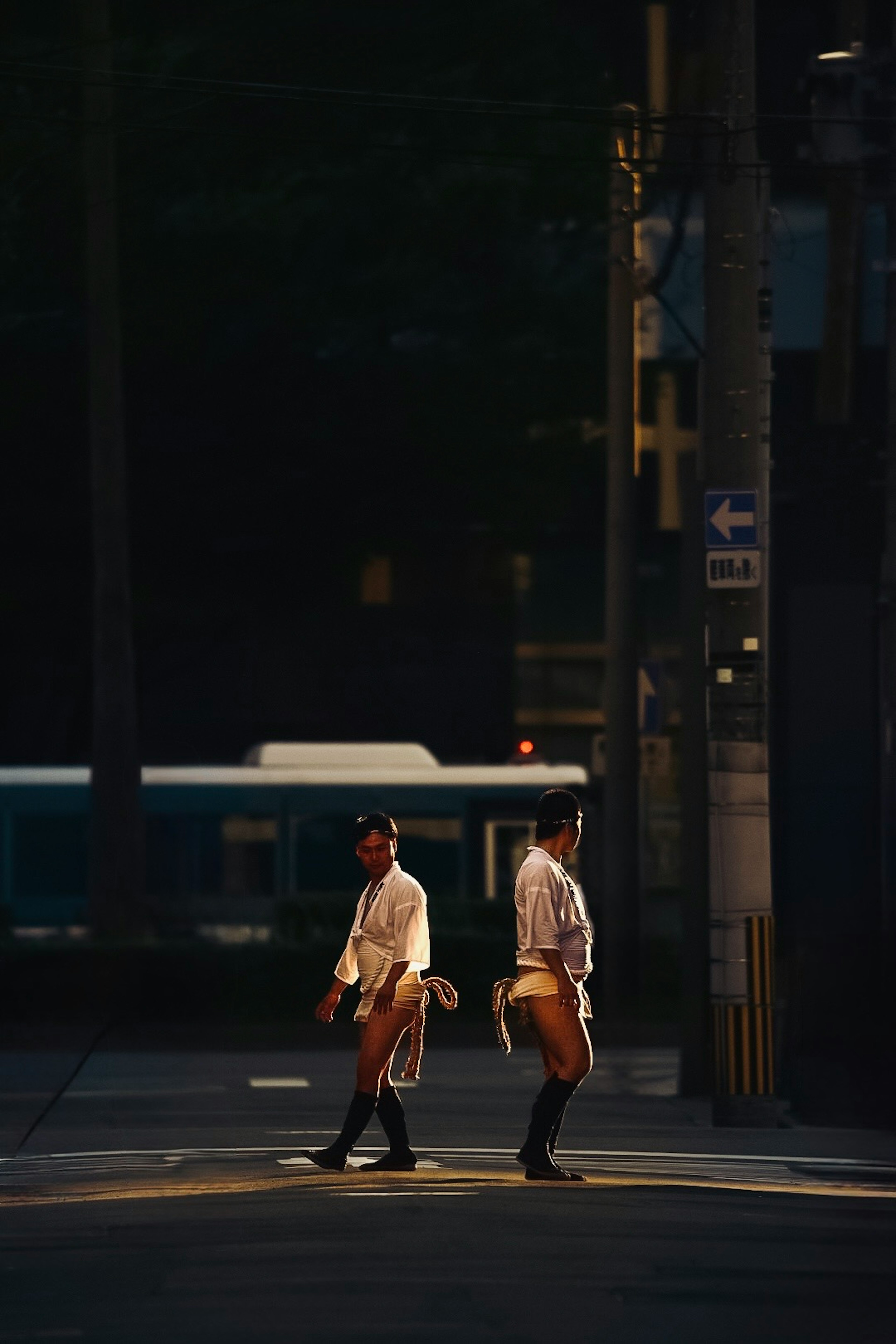 Two figures walking in a nighttime urban setting with a train in the background