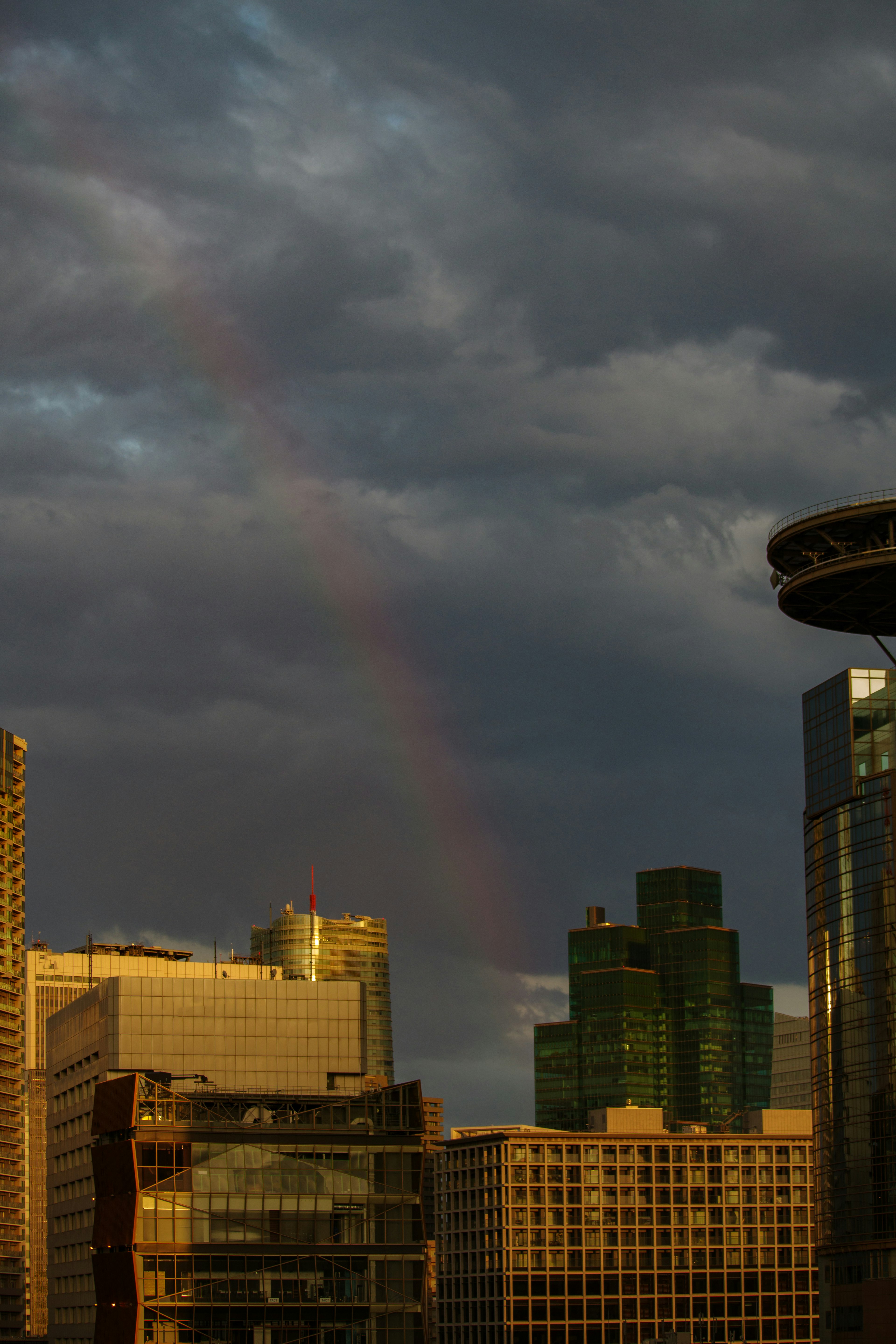 A rainbow appearing between buildings under dark clouds