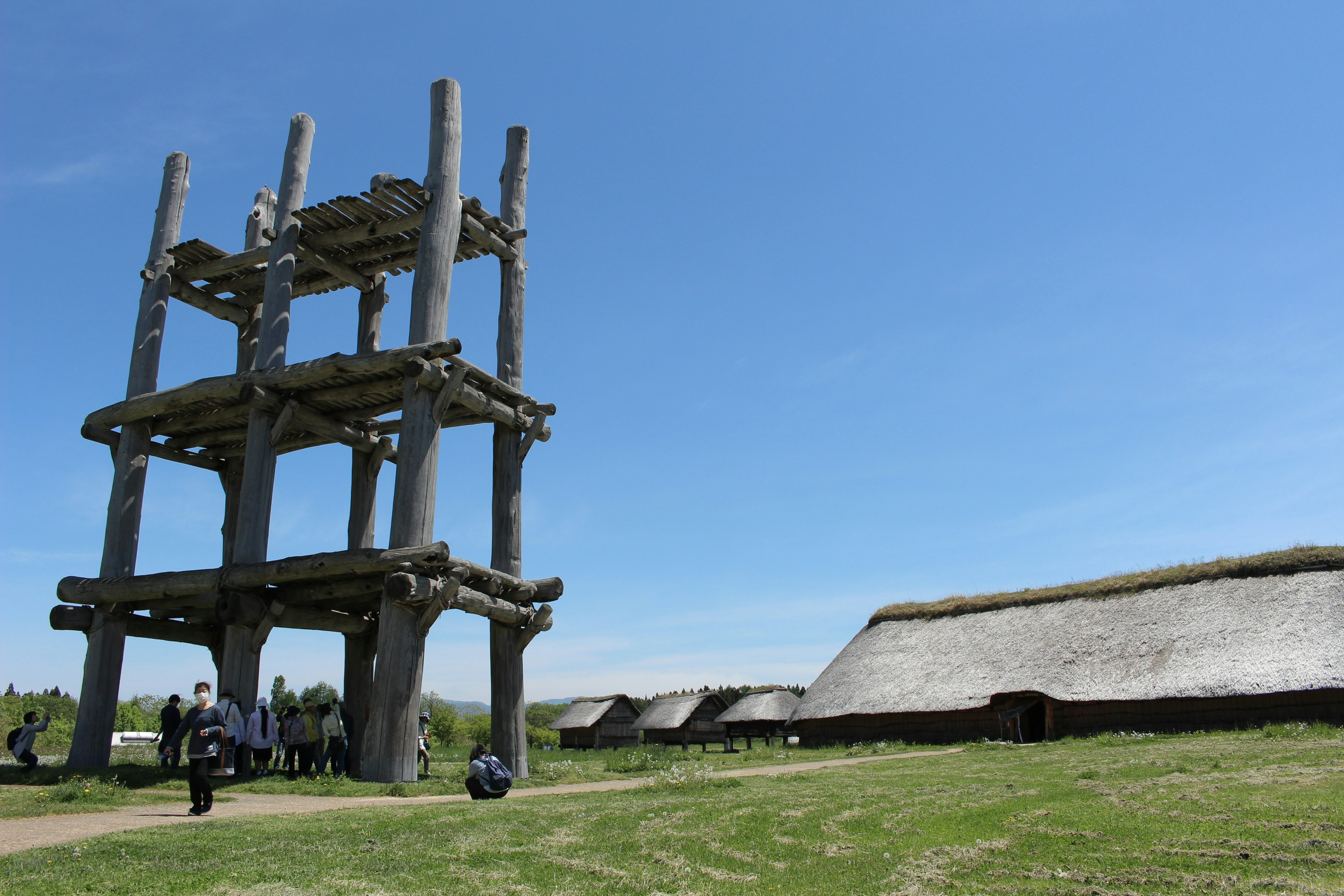 Alte Holzkonstruktion unter blauem Himmel mit traditionellen Häusern auf der Wiese