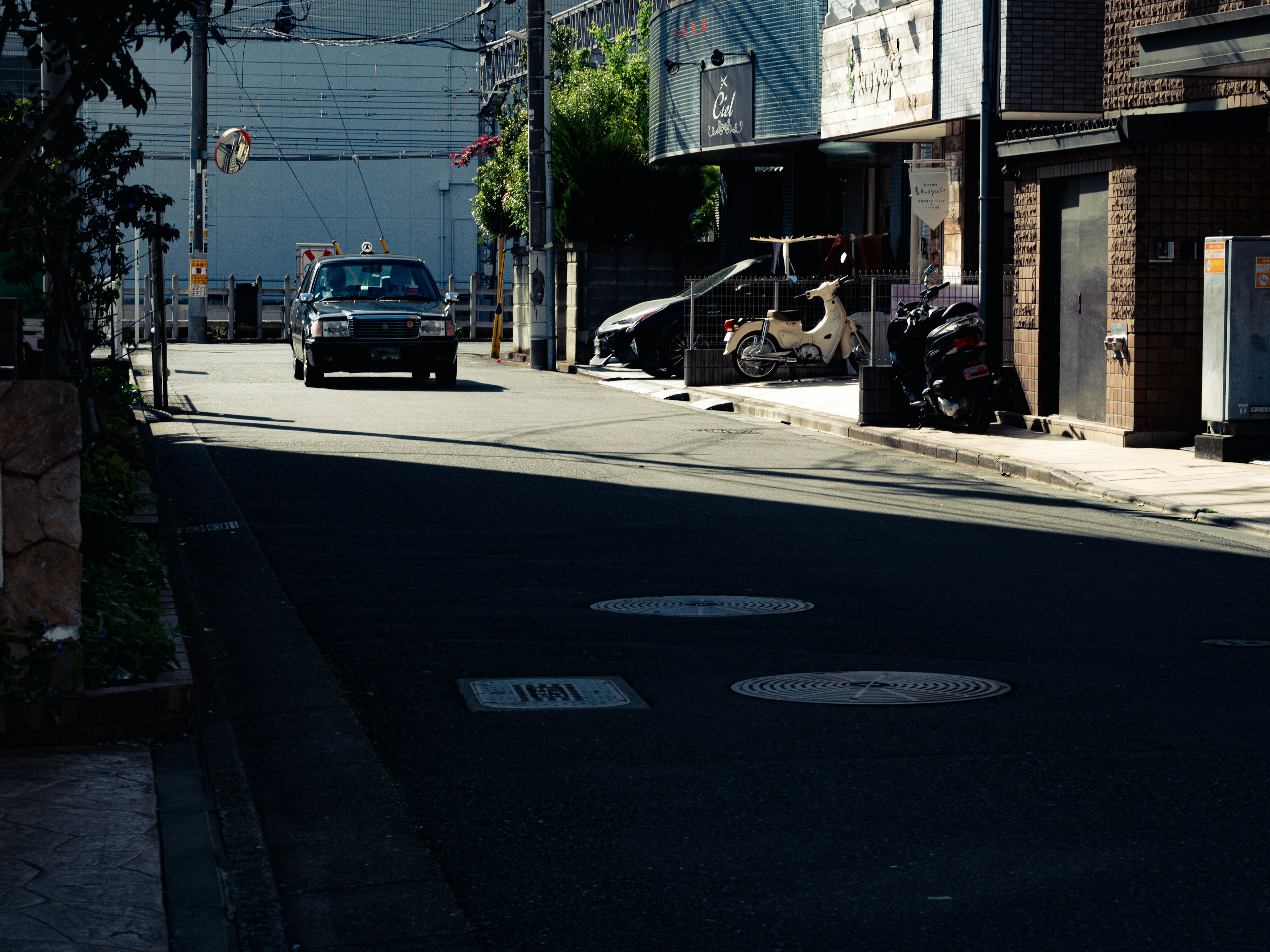 Un coche conduciendo por una calle tranquila con edificios y sombras