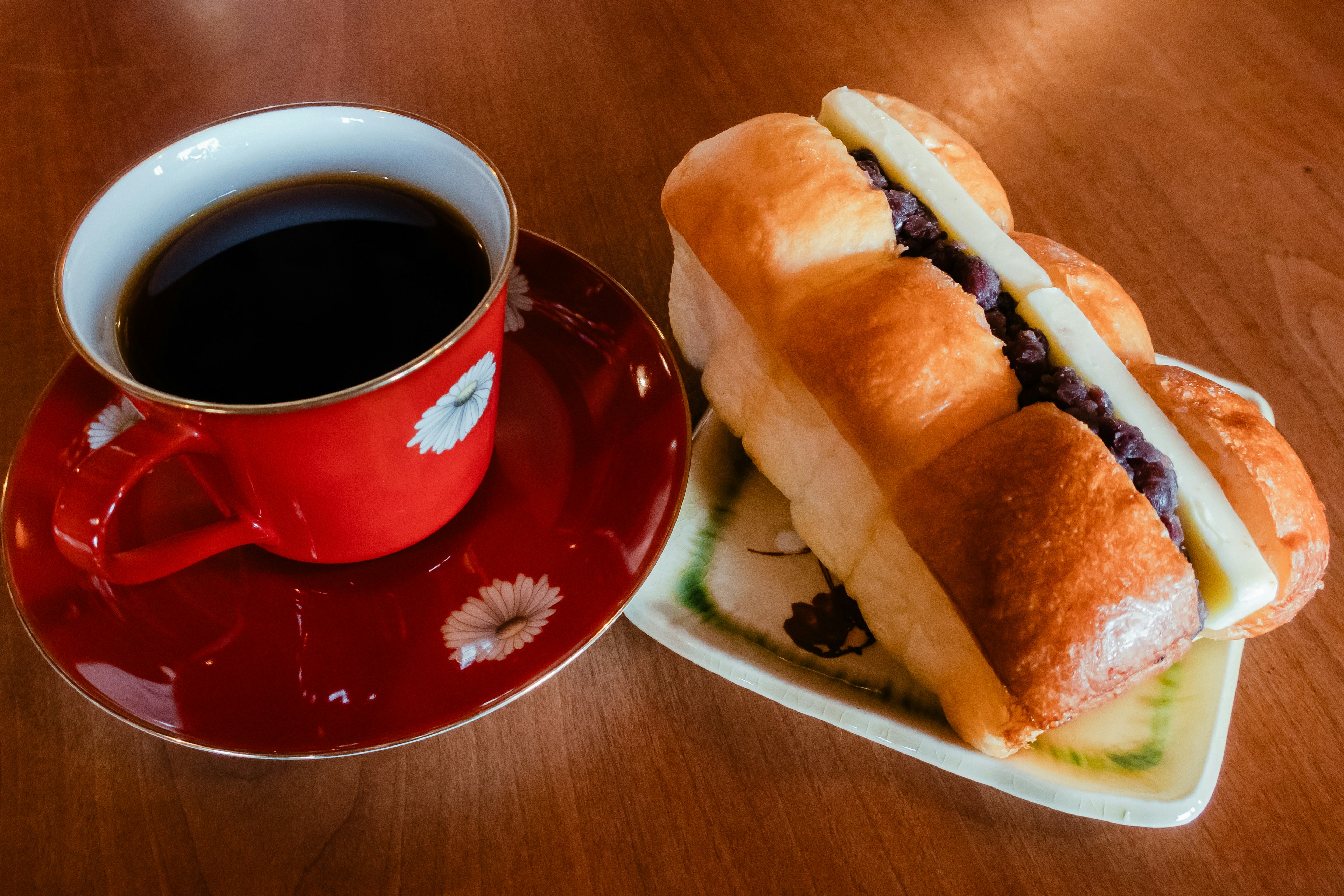 Eine Tasse Kaffee neben einem süßen Brot gefüllt mit roter Bohnenpaste