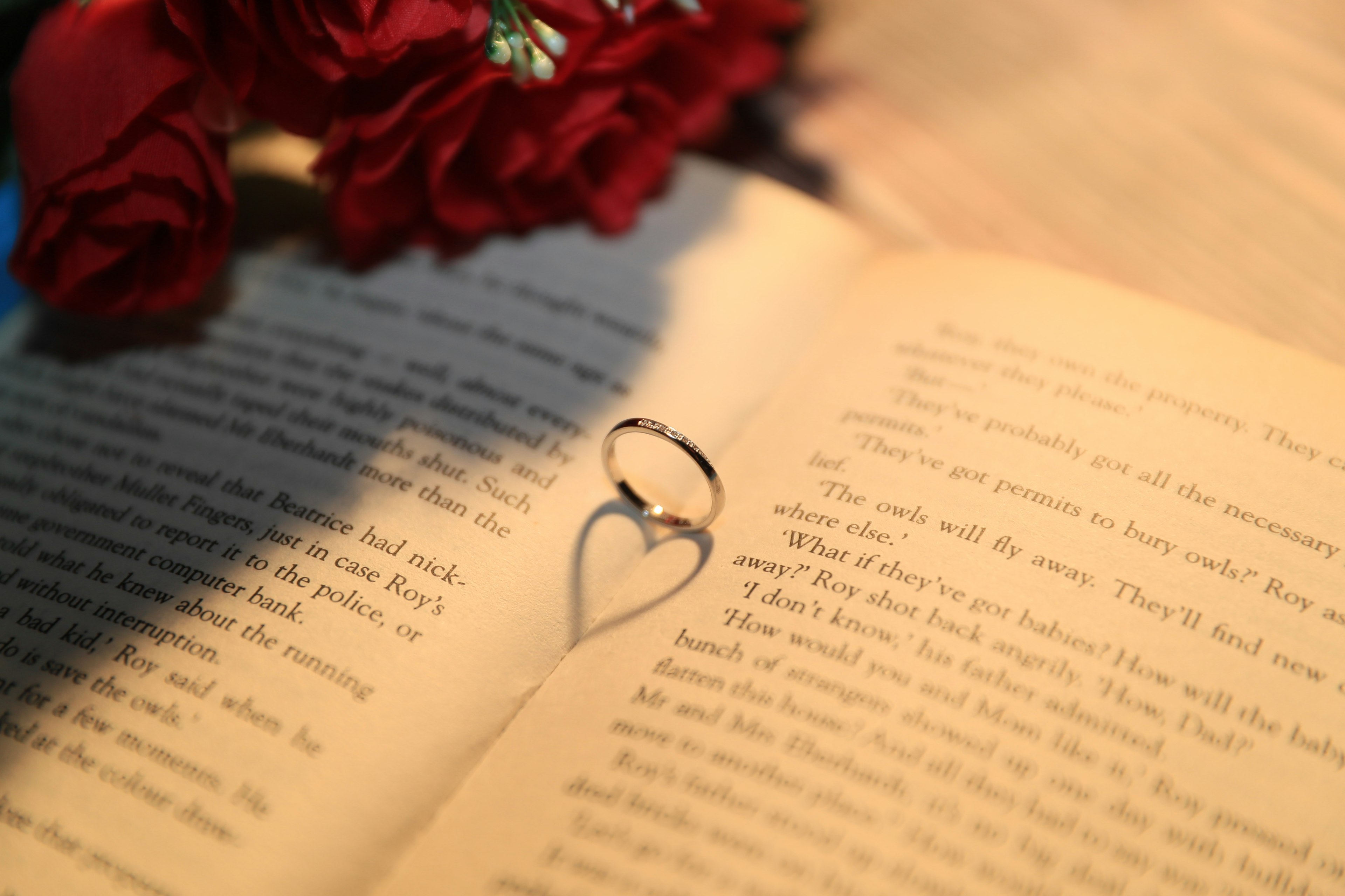 Une bague en forme de cœur posée sur une page de livre ouverte avec des roses rouges en arrière-plan