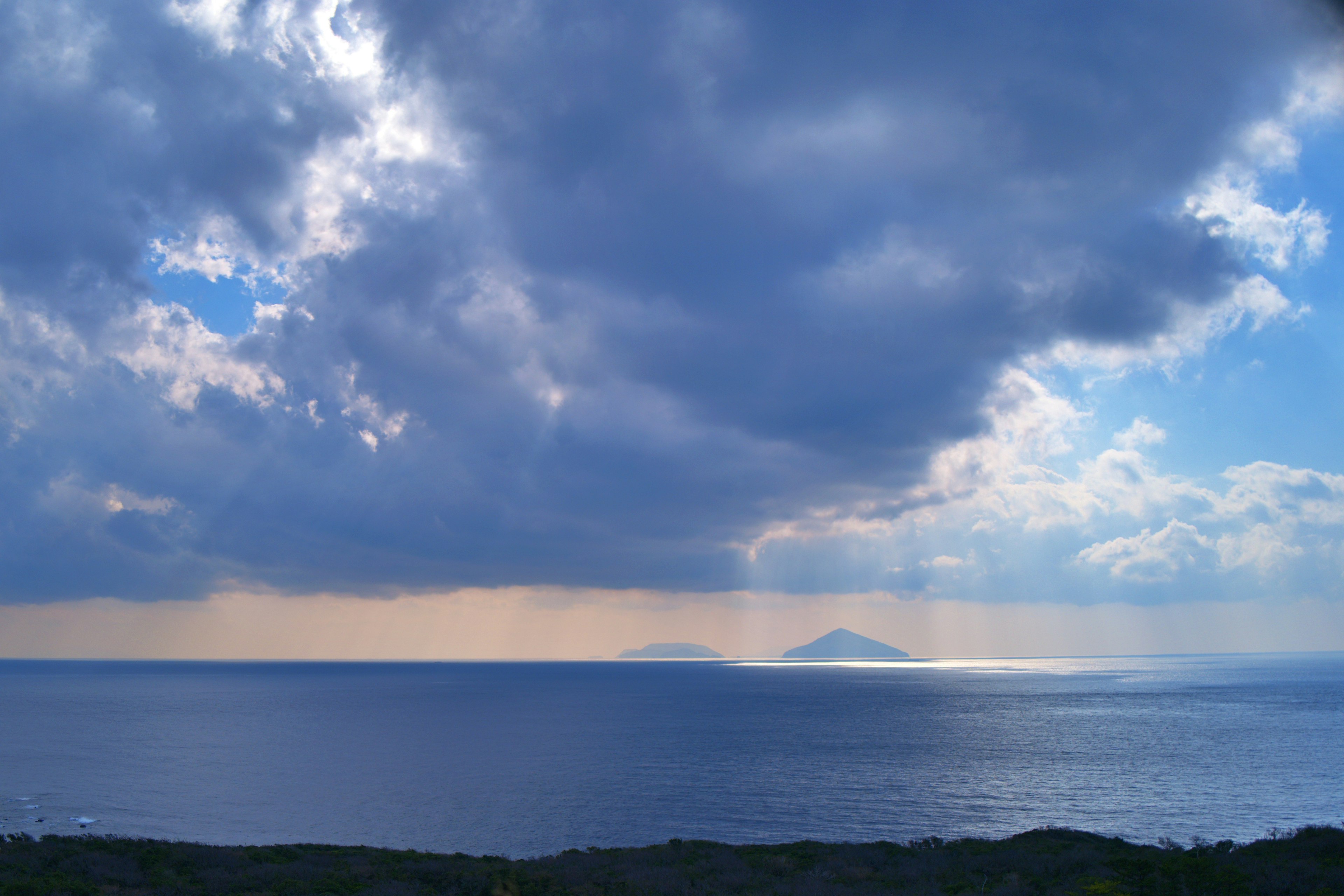 Vista de un mar azul con nubes e islas pequeñas a lo lejos