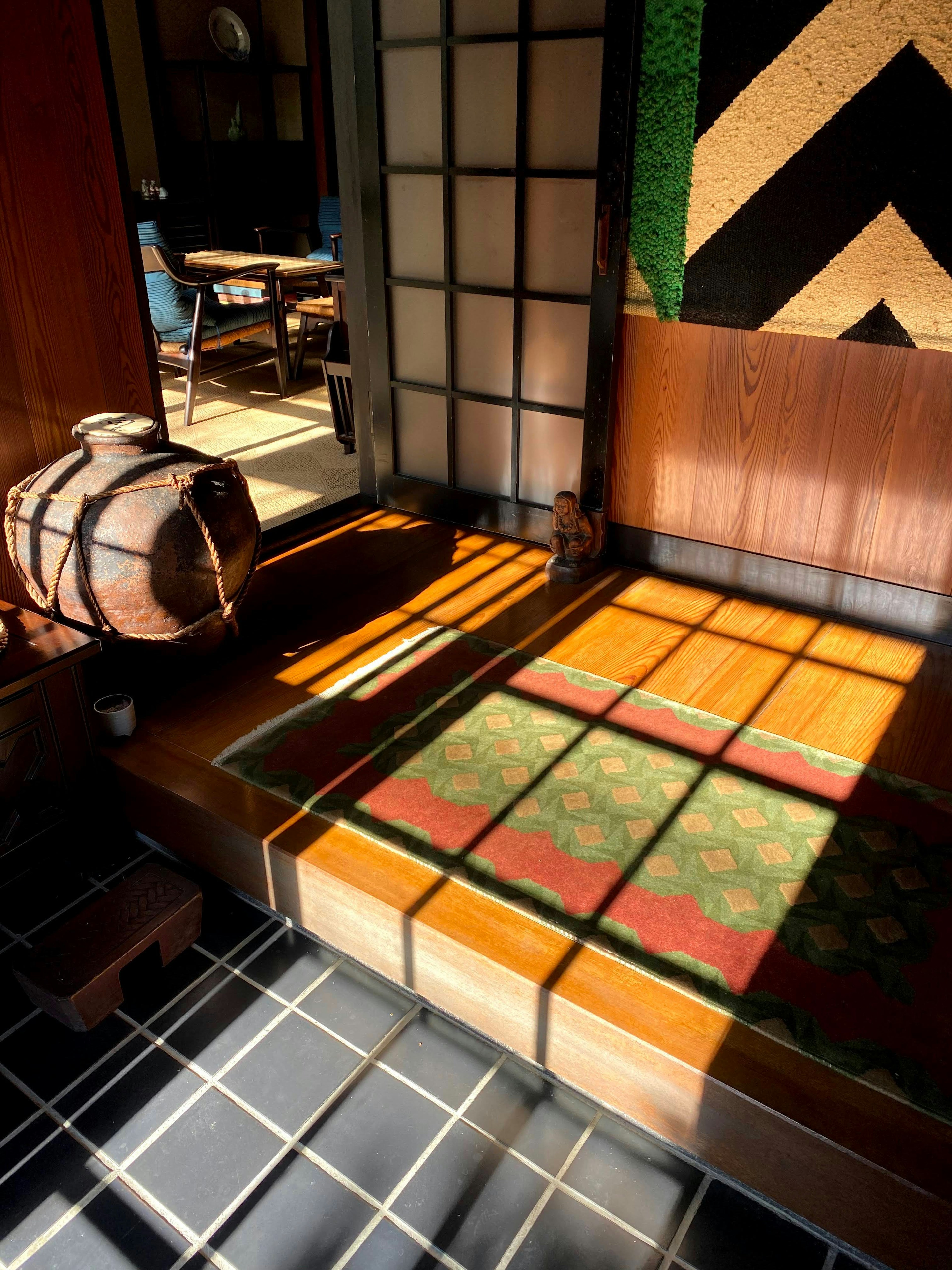 A corner of a traditional Japanese room with wooden cushions and a ceramic jar illuminated by bright light