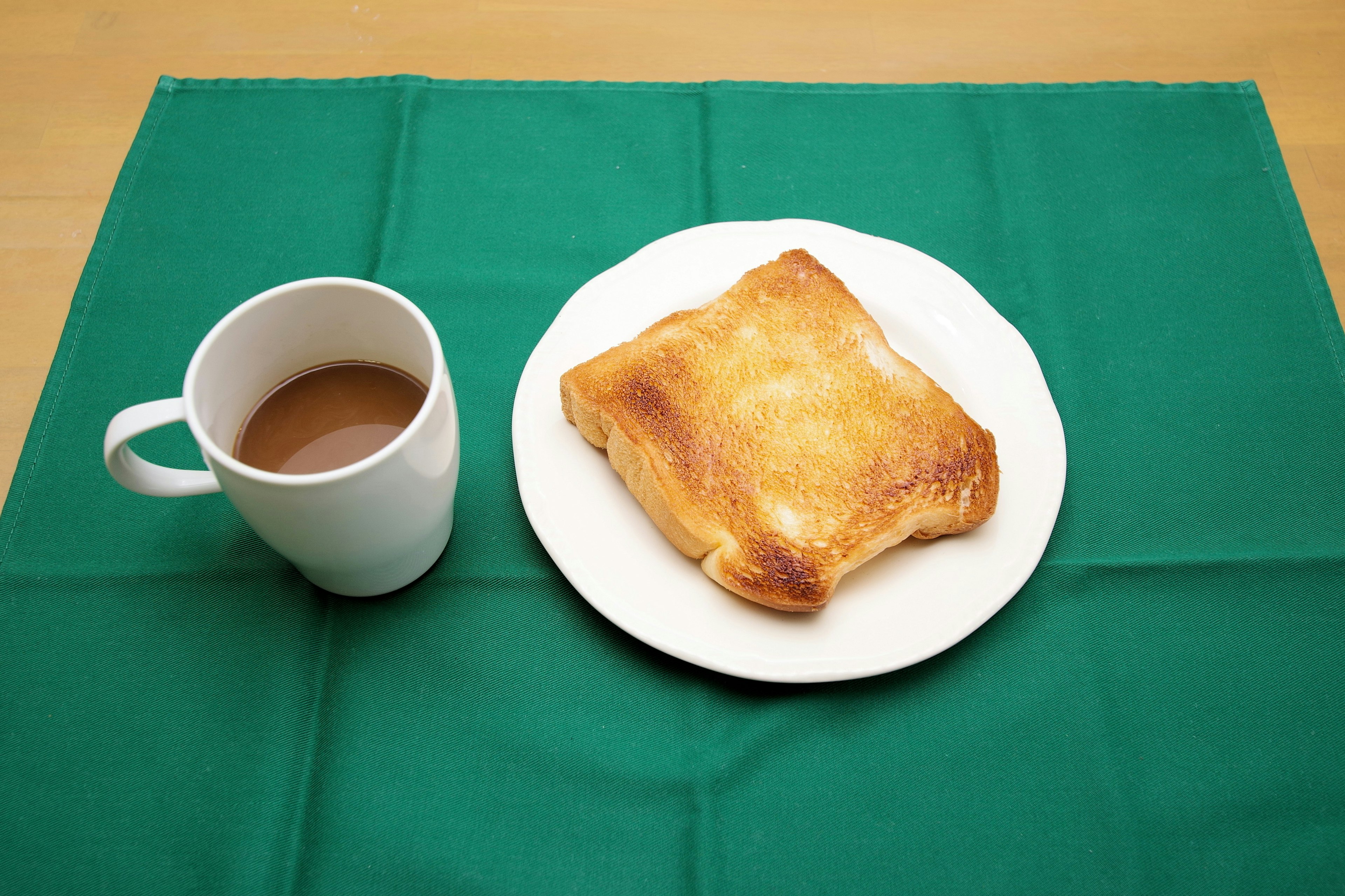 Tostada en un plato blanco junto a una taza de café sobre un mantel verde