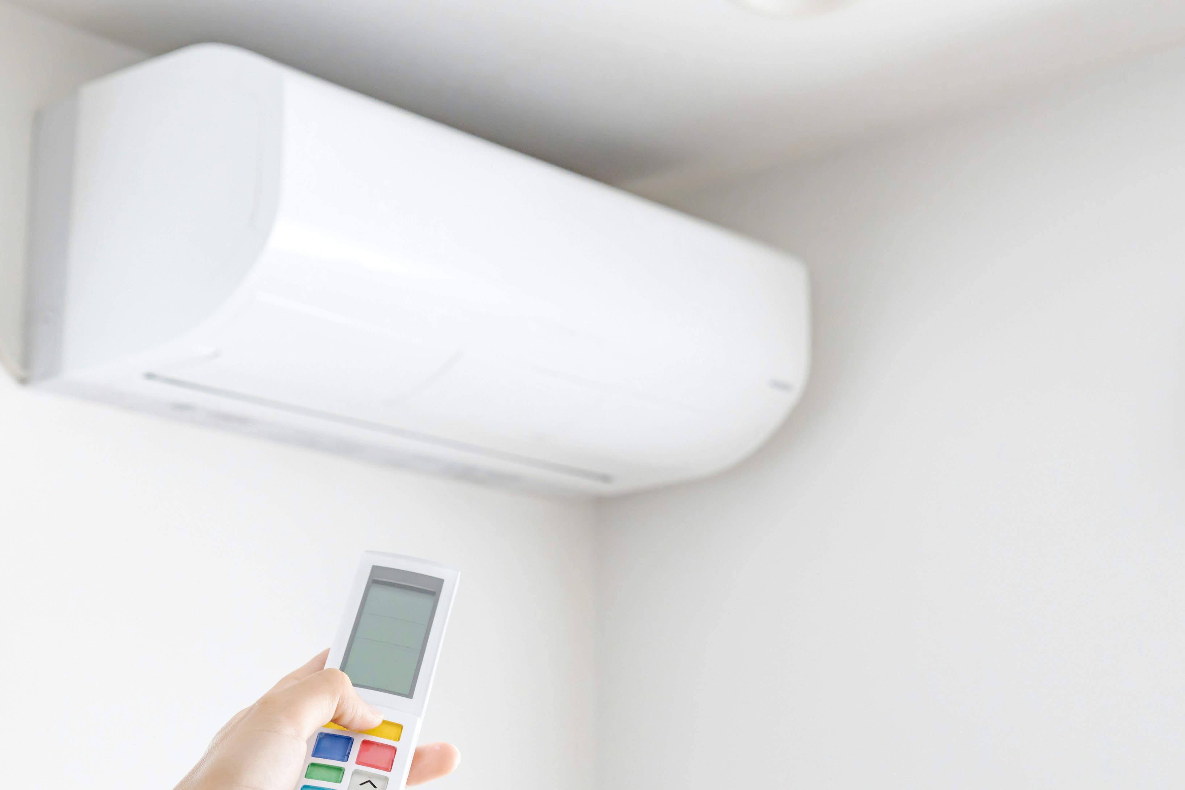 Air conditioner mounted on a wall with a remote control in hand