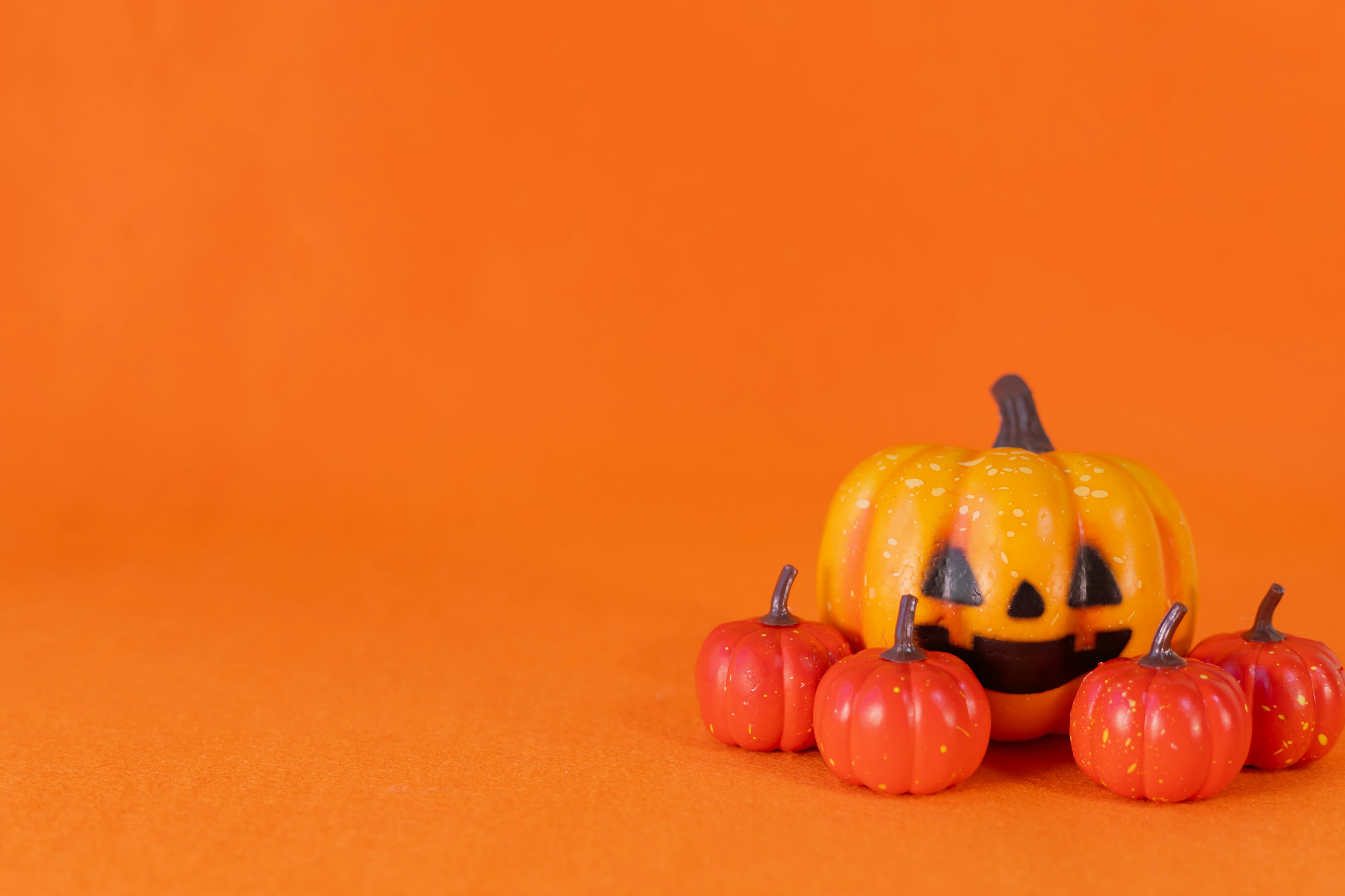 Una calabaza tallada rodeada de pequeñas calabazas rojas sobre un fondo naranja