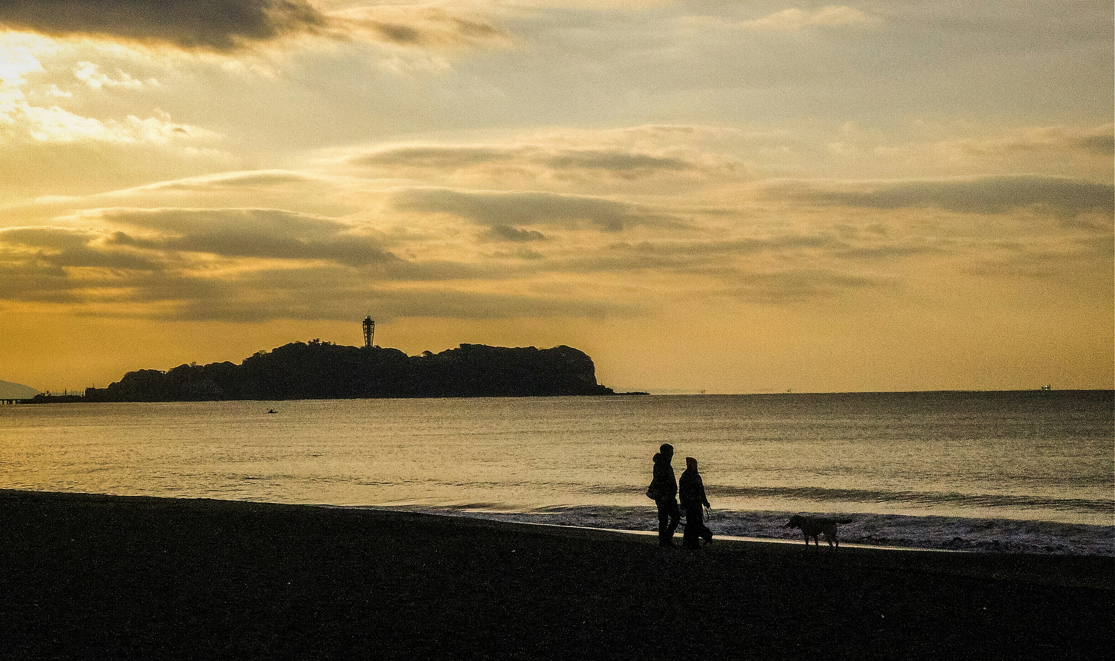 Silhouette eines Paares, das mit einem Hund am Strand bei Sonnenuntergang spazieren geht