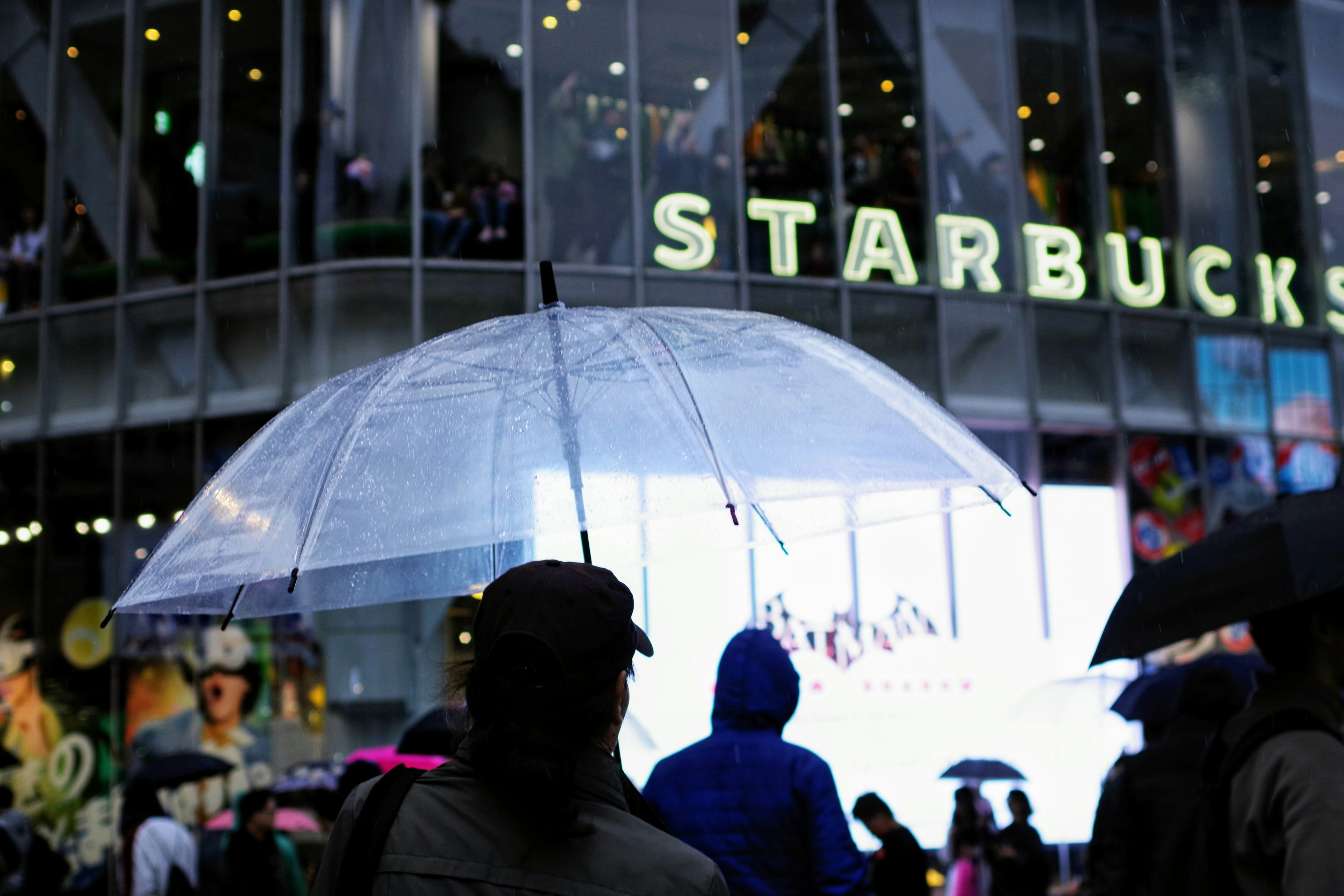 Personas con un paraguas transparente frente a un Starbucks por la noche