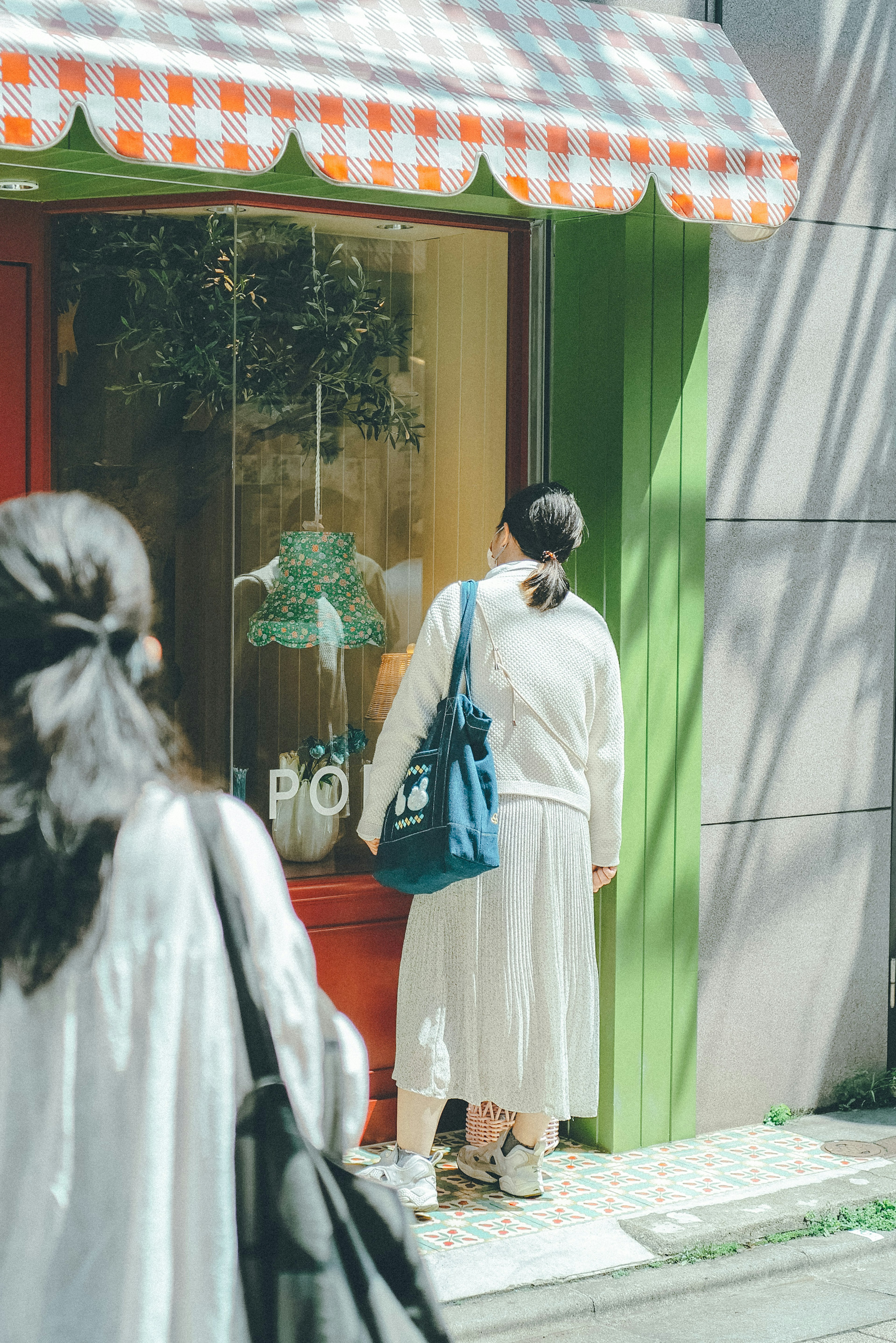 A woman standing in front of a shop with a green wall and an orange and white checkered awning