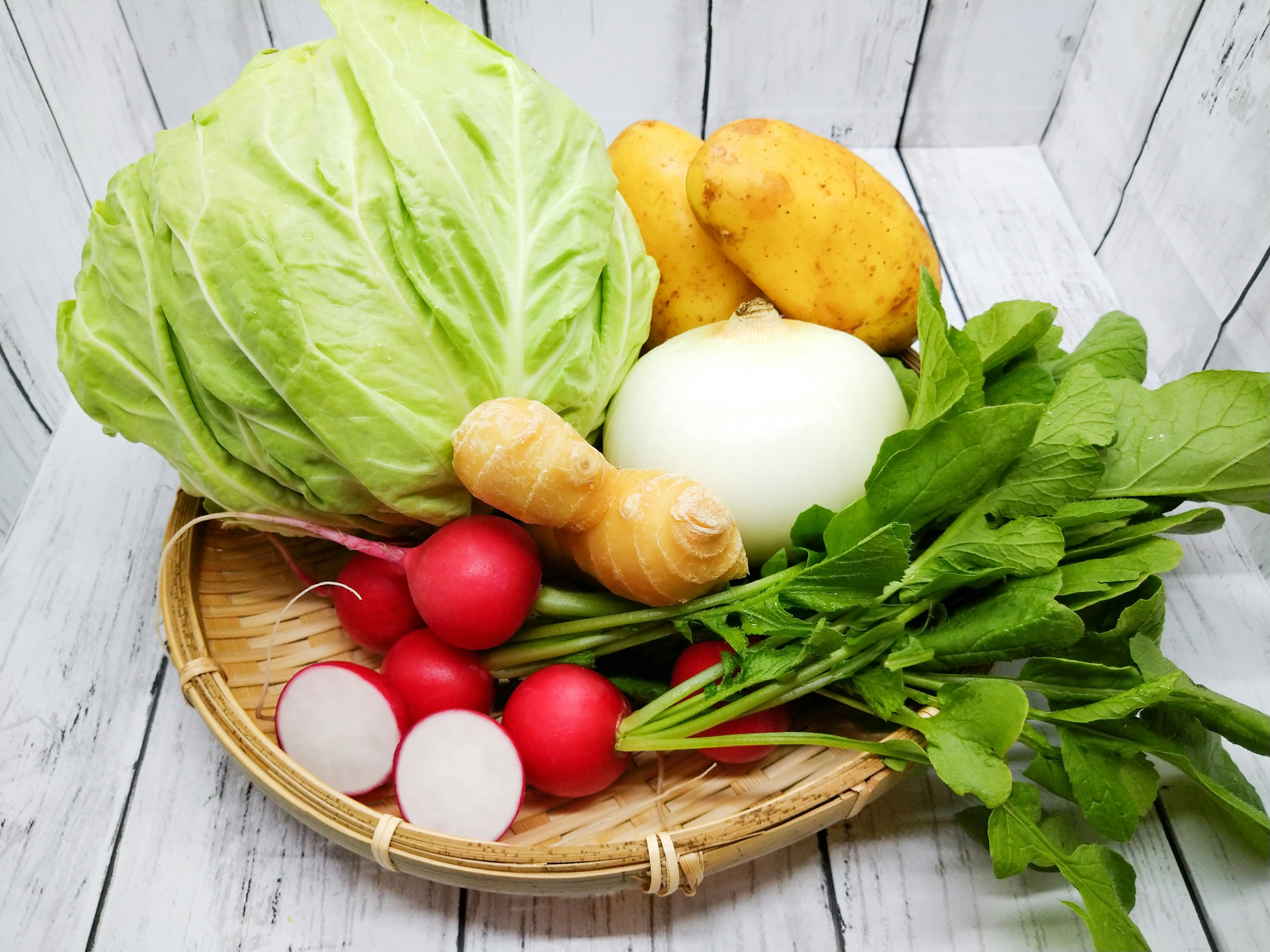 Asortimento fresco de verduras que incluye repollo, papas, cebolla, rábanos, verduras y jengibre en una canasta