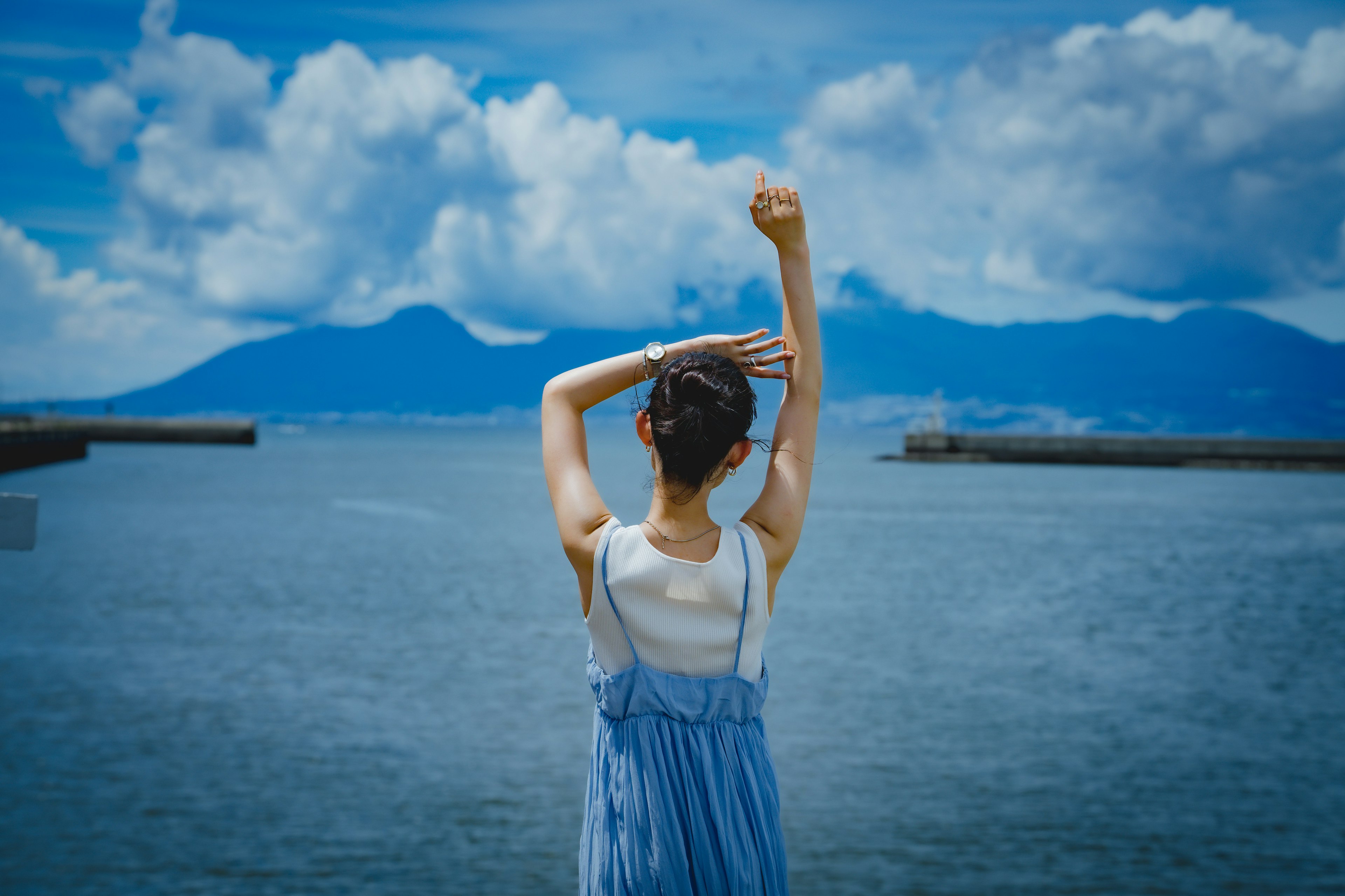 A woman gazing at the sea with her back to the camera blue sky and clouds in the background