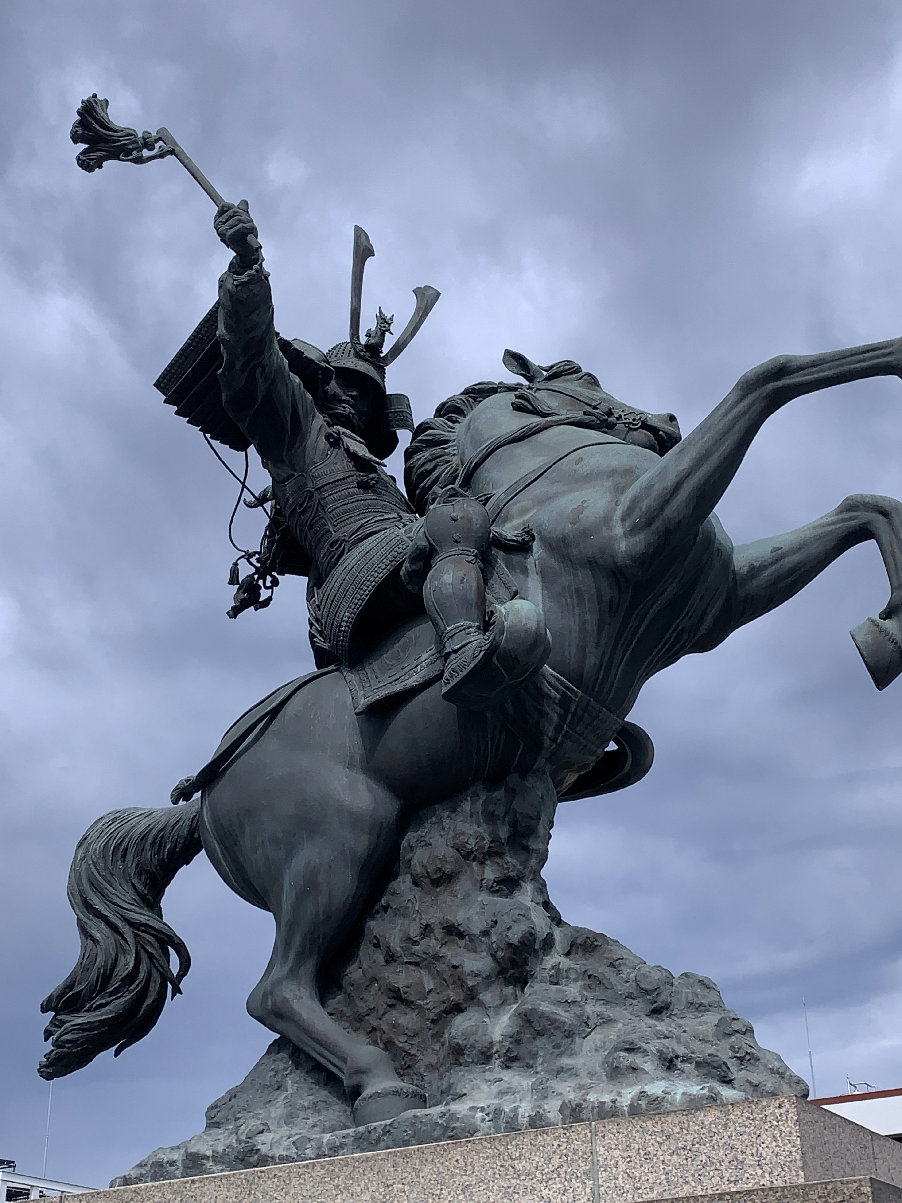 Bronze statue of a warrior on horseback holding a sword high under stormy clouds