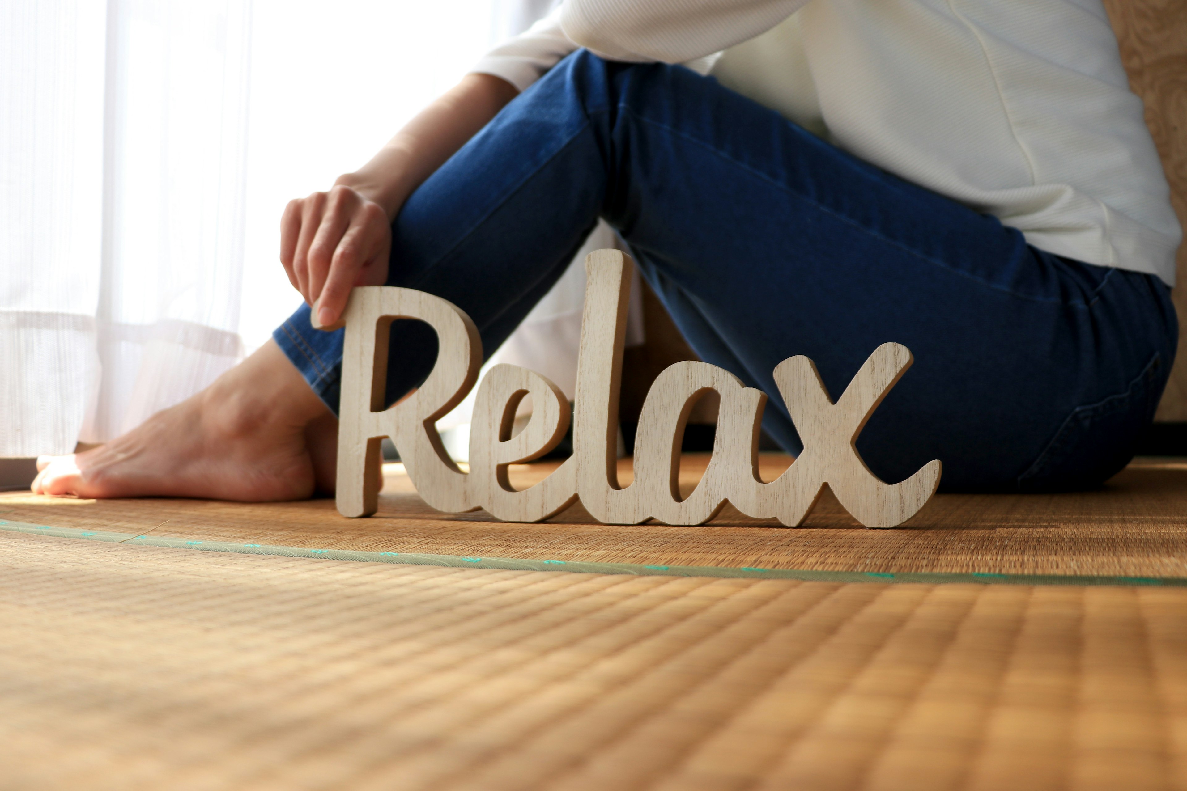 Person, die ein Holzschild mit der Aufschrift Relax hält, mit Füßen auf einem Tatami