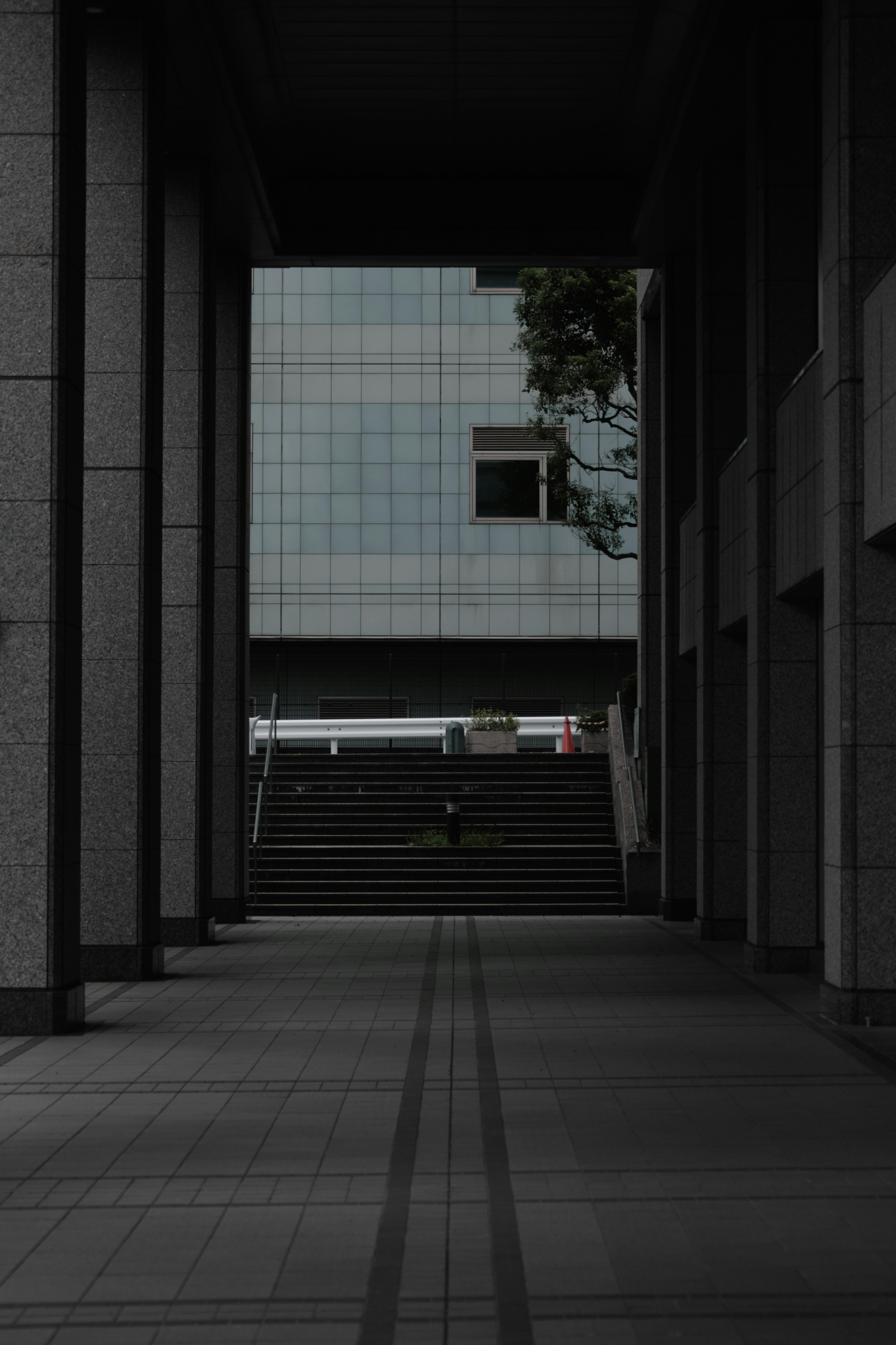 Couloir sombre menant à un bâtiment moderne avec une fenêtre et des escaliers