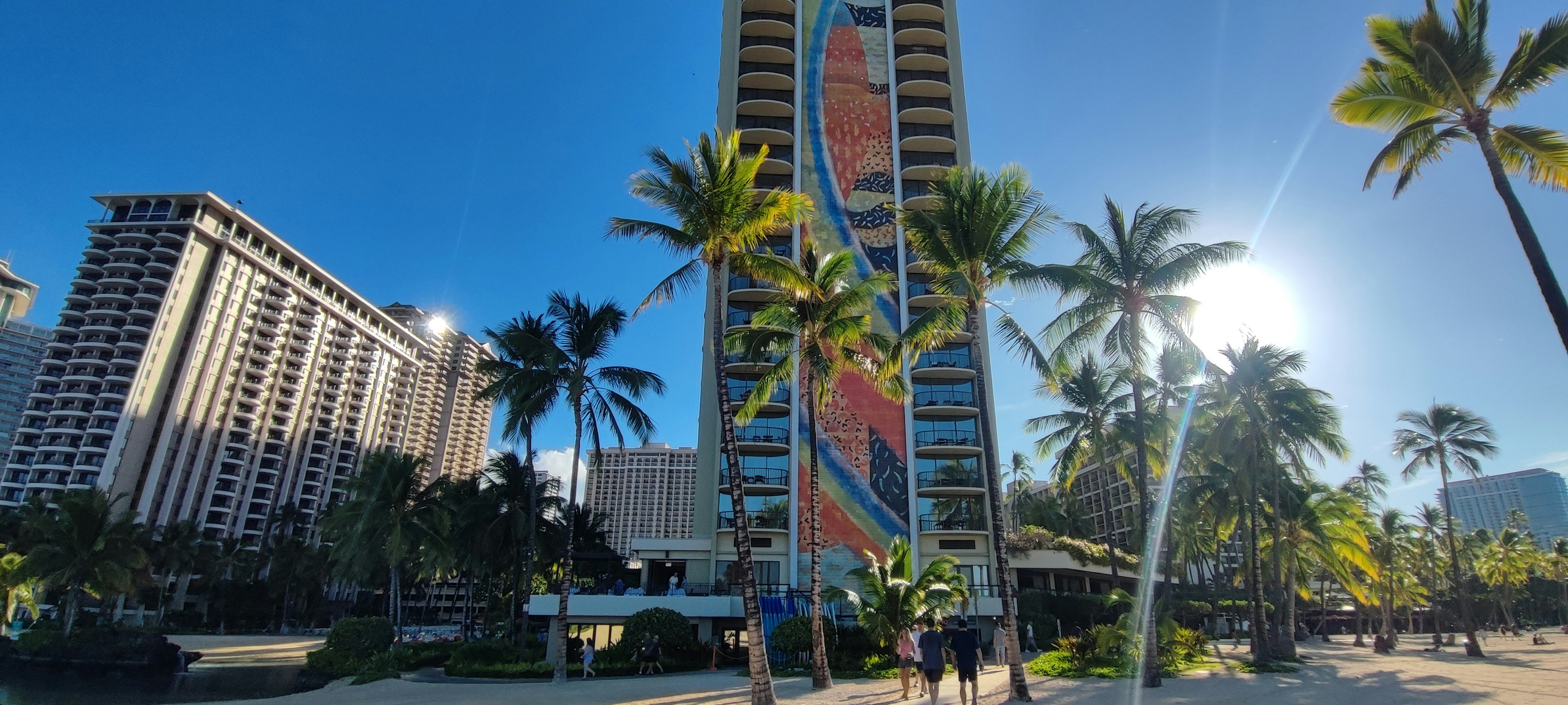 Panoramic view featuring a tall building with a colorful mural surrounded by palm trees and blue sky