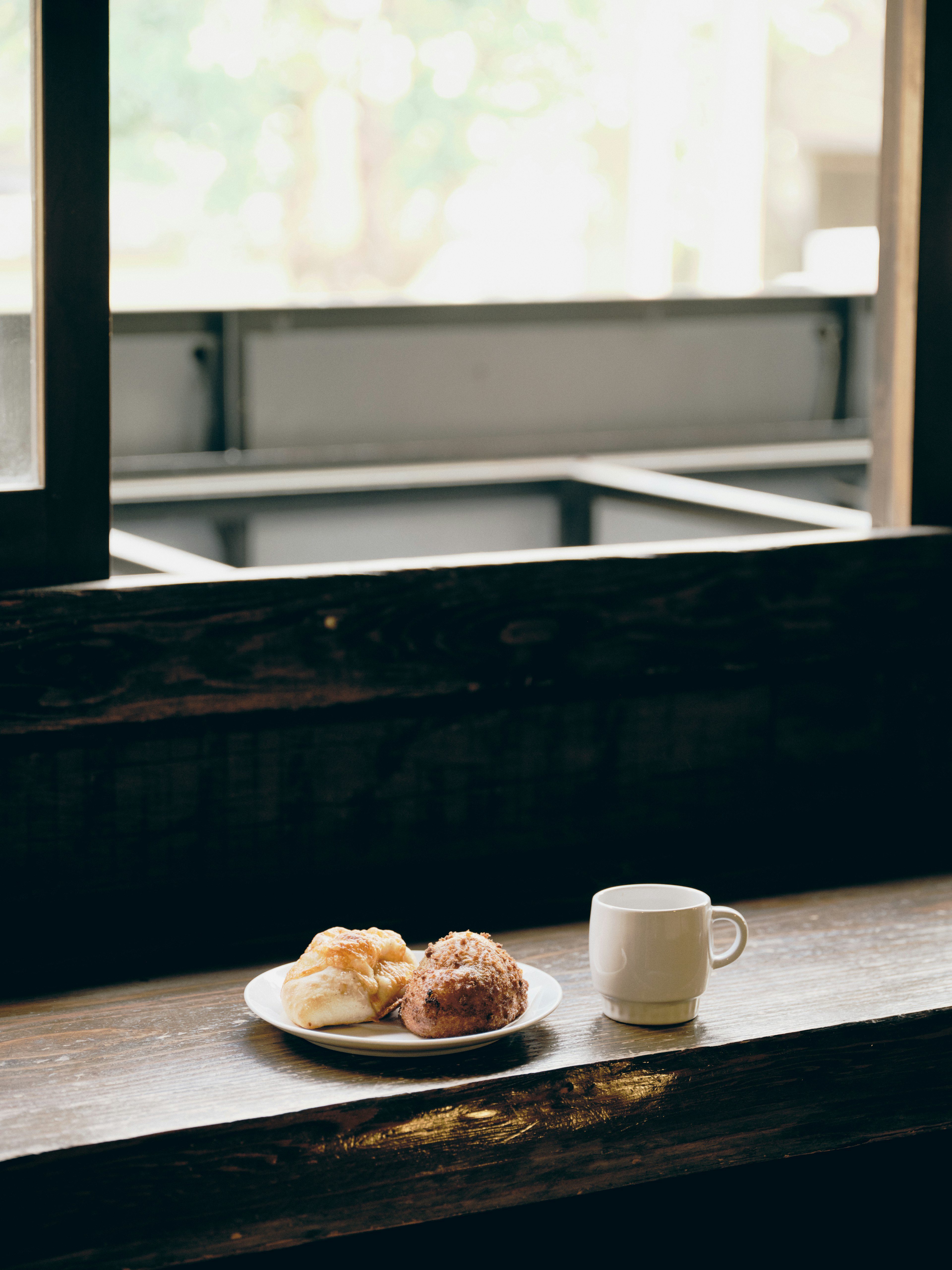 A white cup and pastries on a plate placed by a window