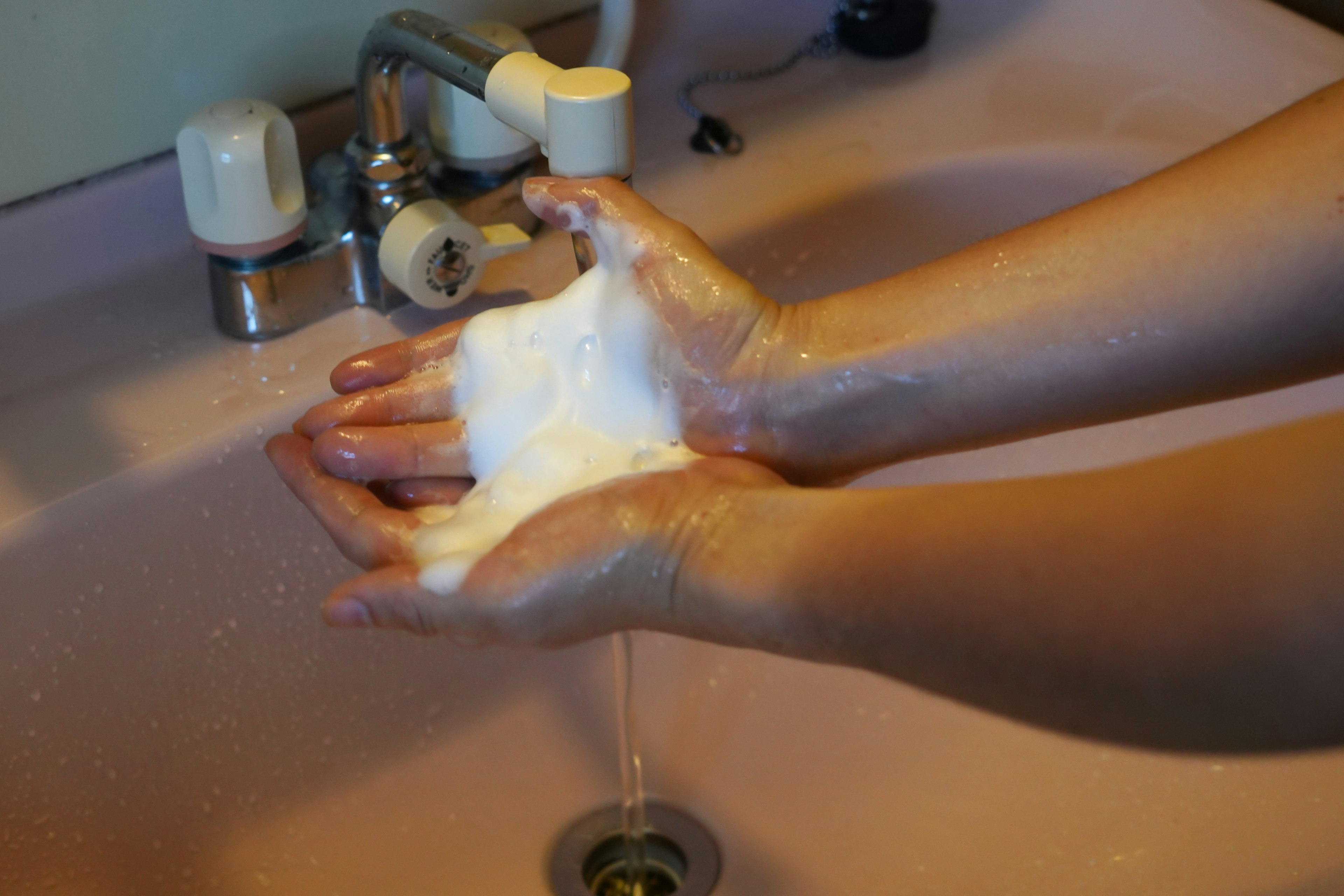 Hands holding soap foam in front of a bathroom sink