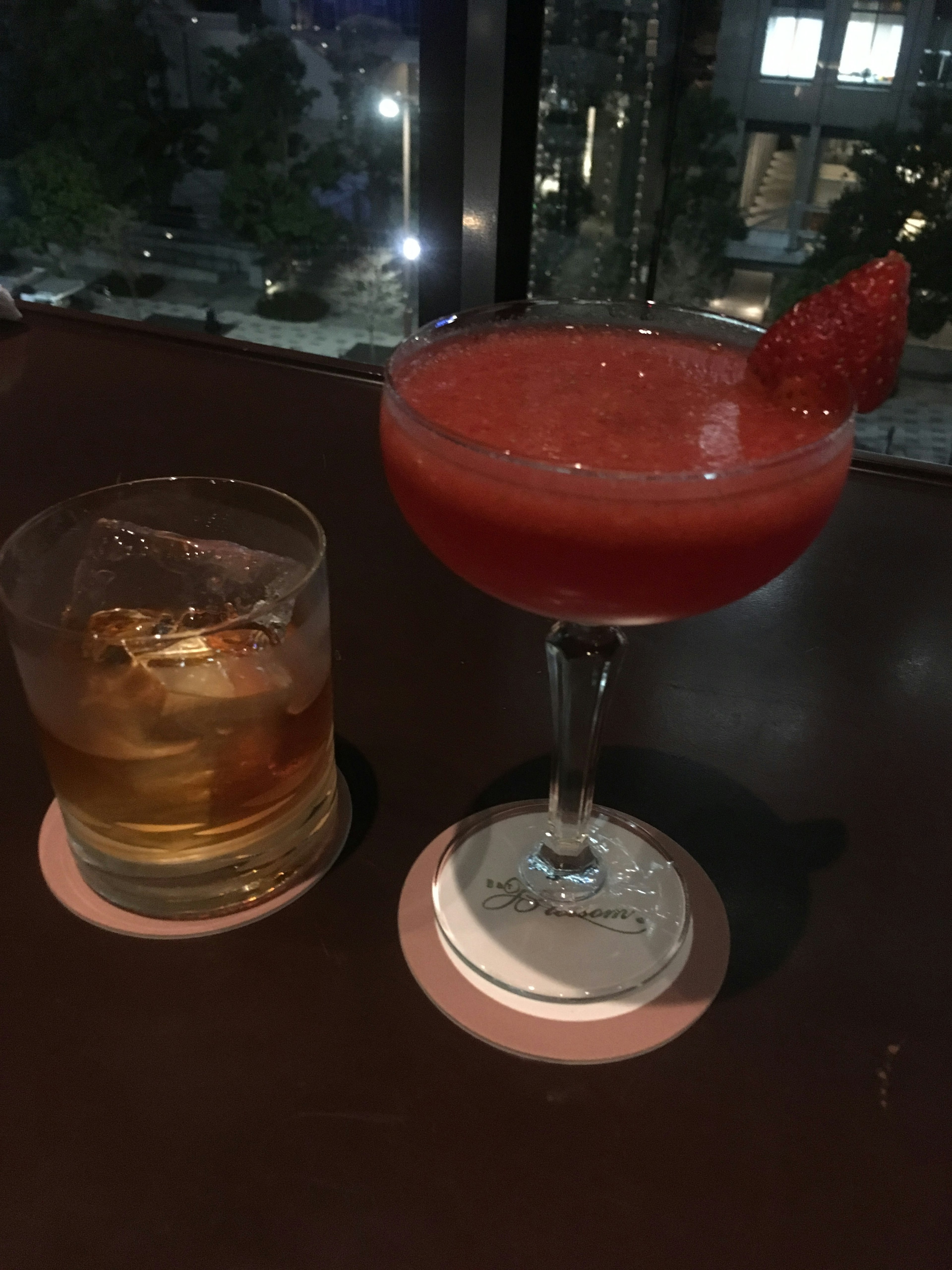 Cocktail and whiskey glass on a table with a nighttime view