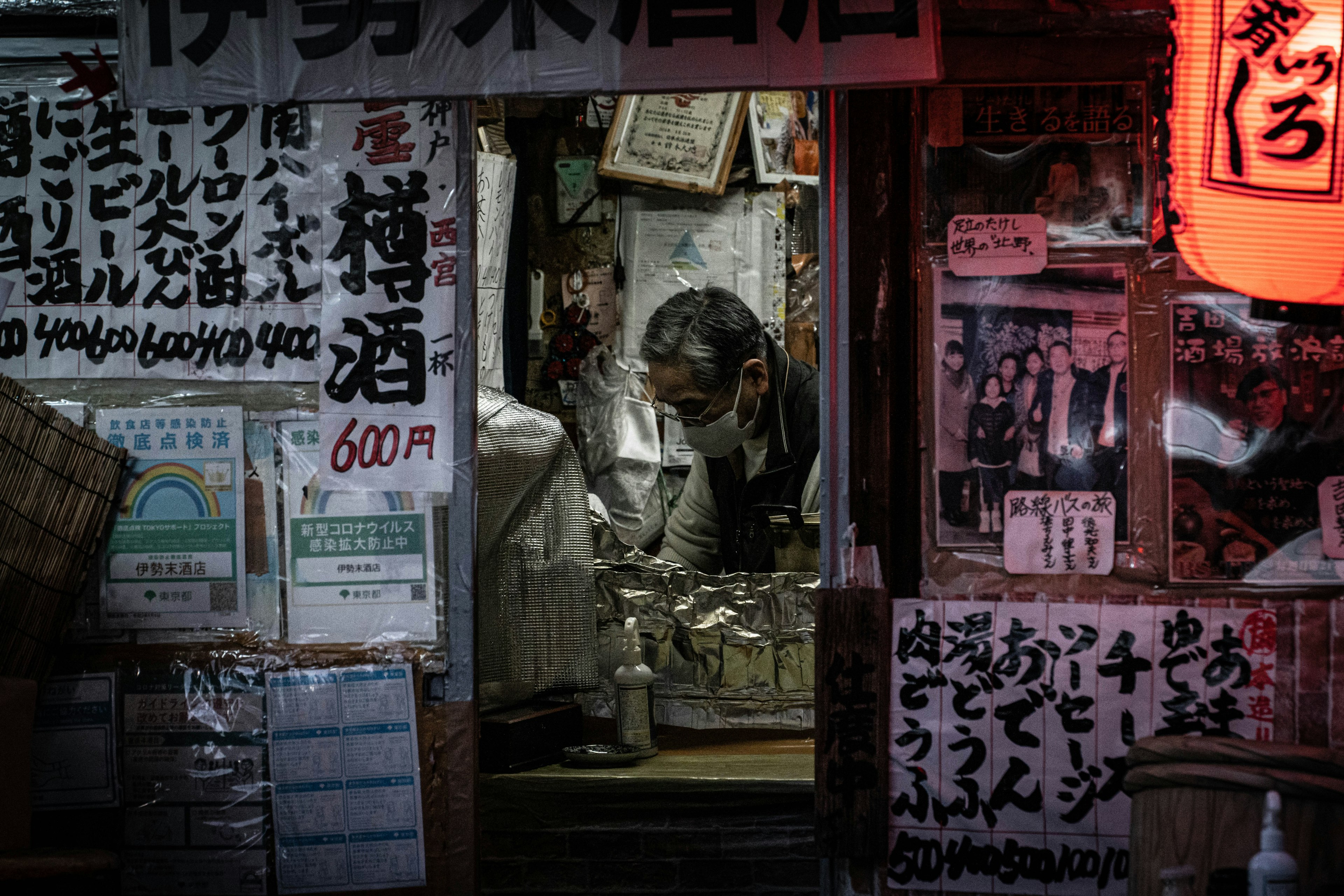 A small sake shop owner preparing products in a dimly lit corner of the street