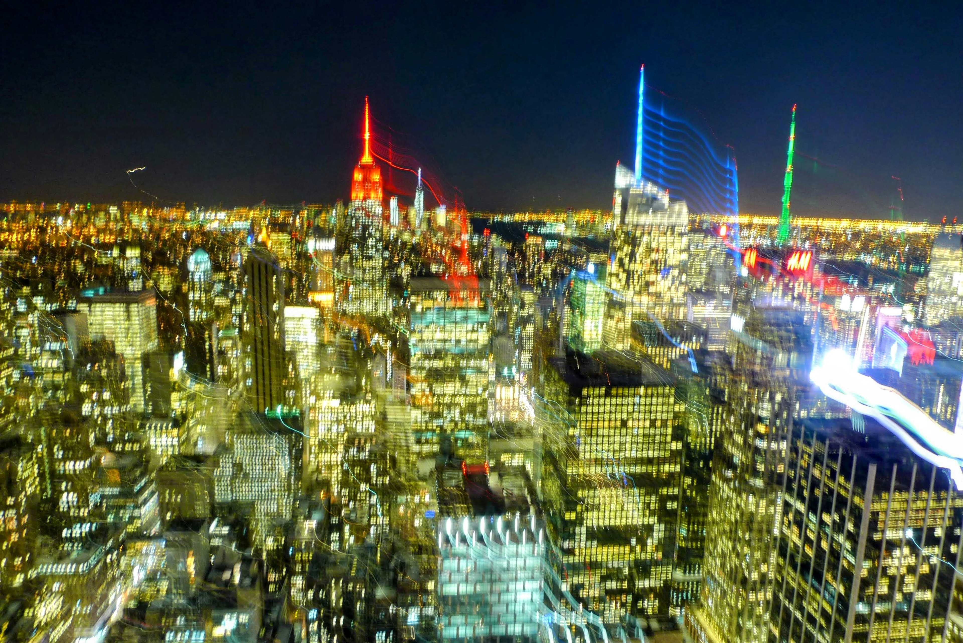 Panoramic view of New York City at night featuring the Empire State Building's red lights and sparkling skyscrapers