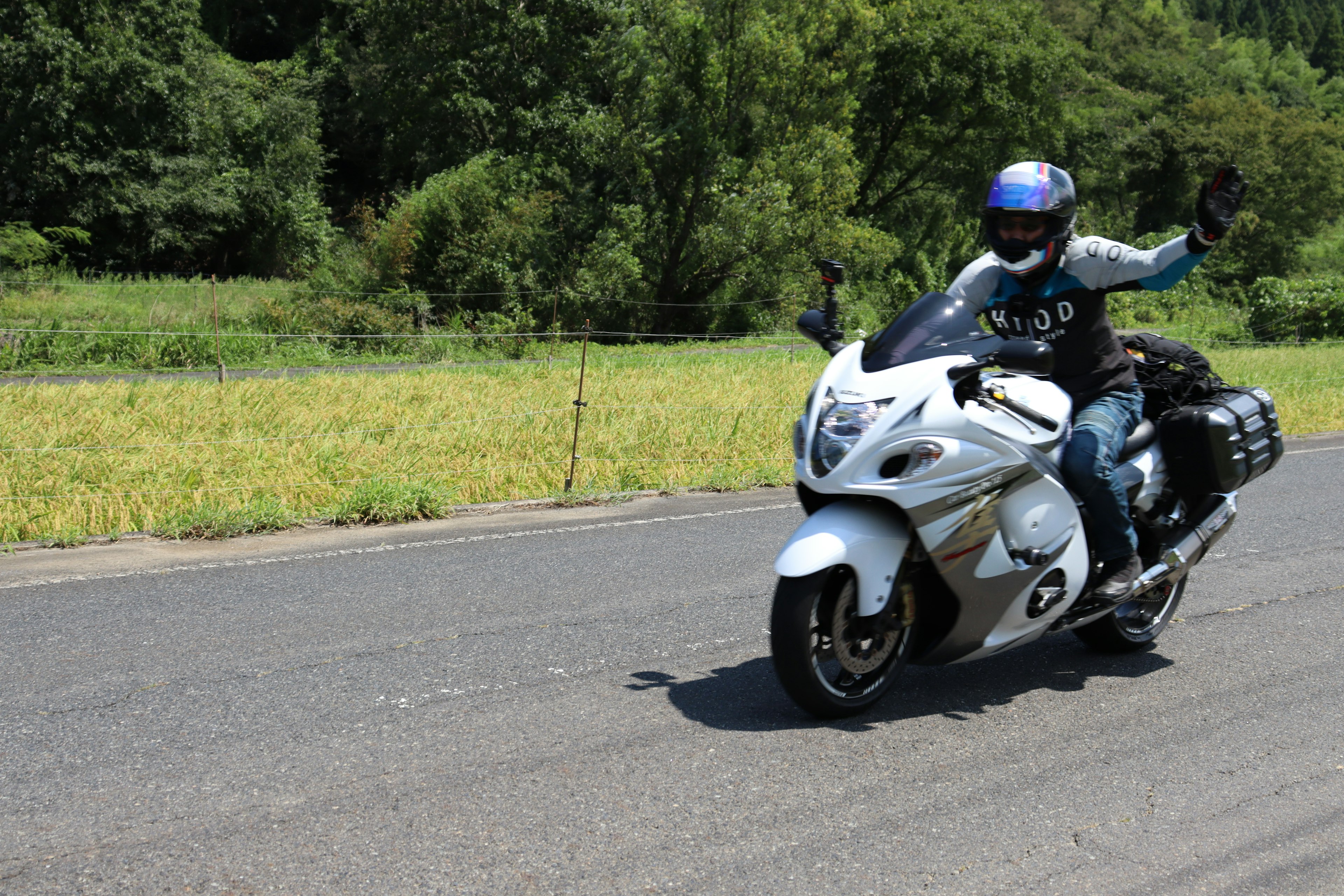 A rider waving while riding a white motorcycle on a sunny road