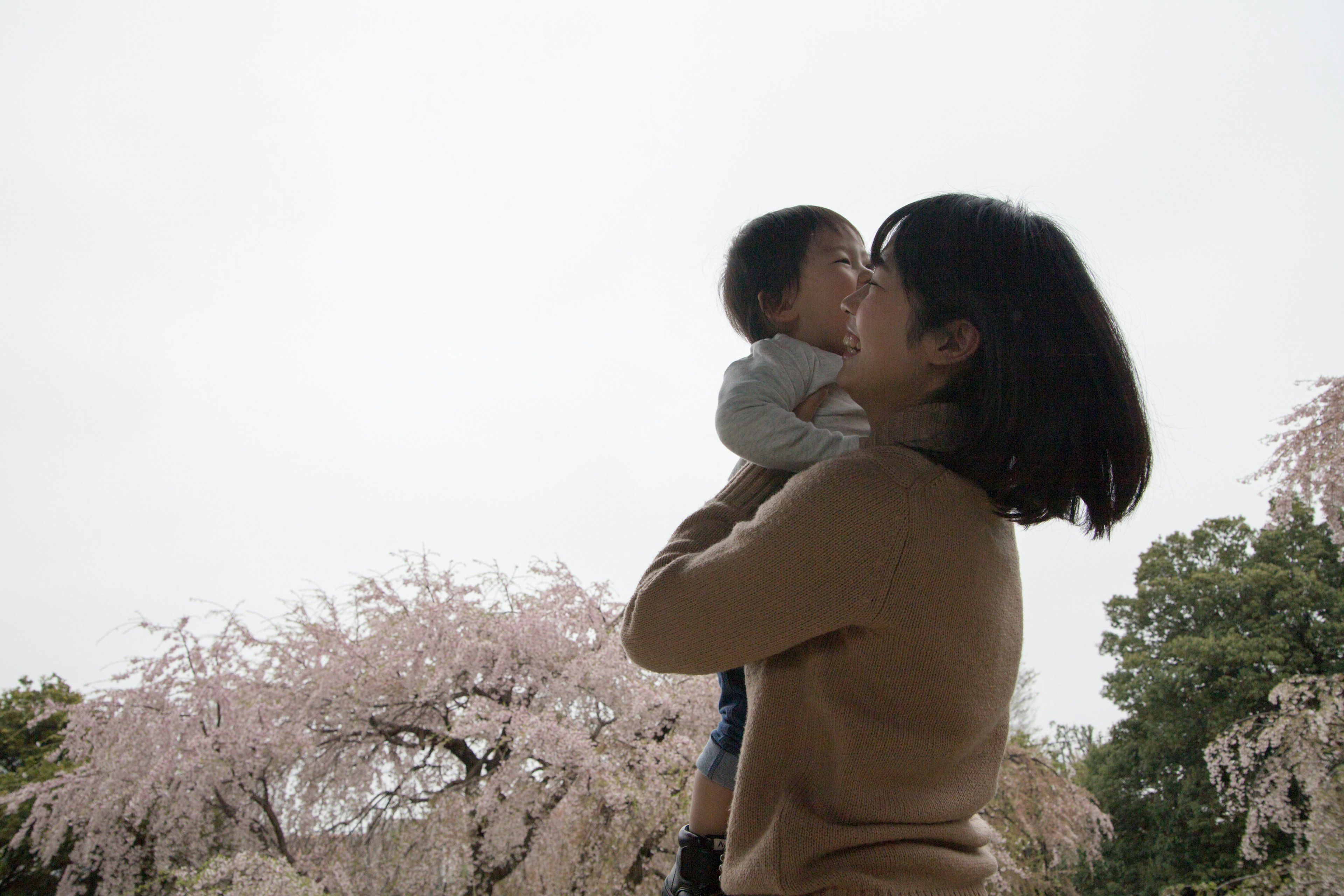 Mother holding her child under cherry blossom trees