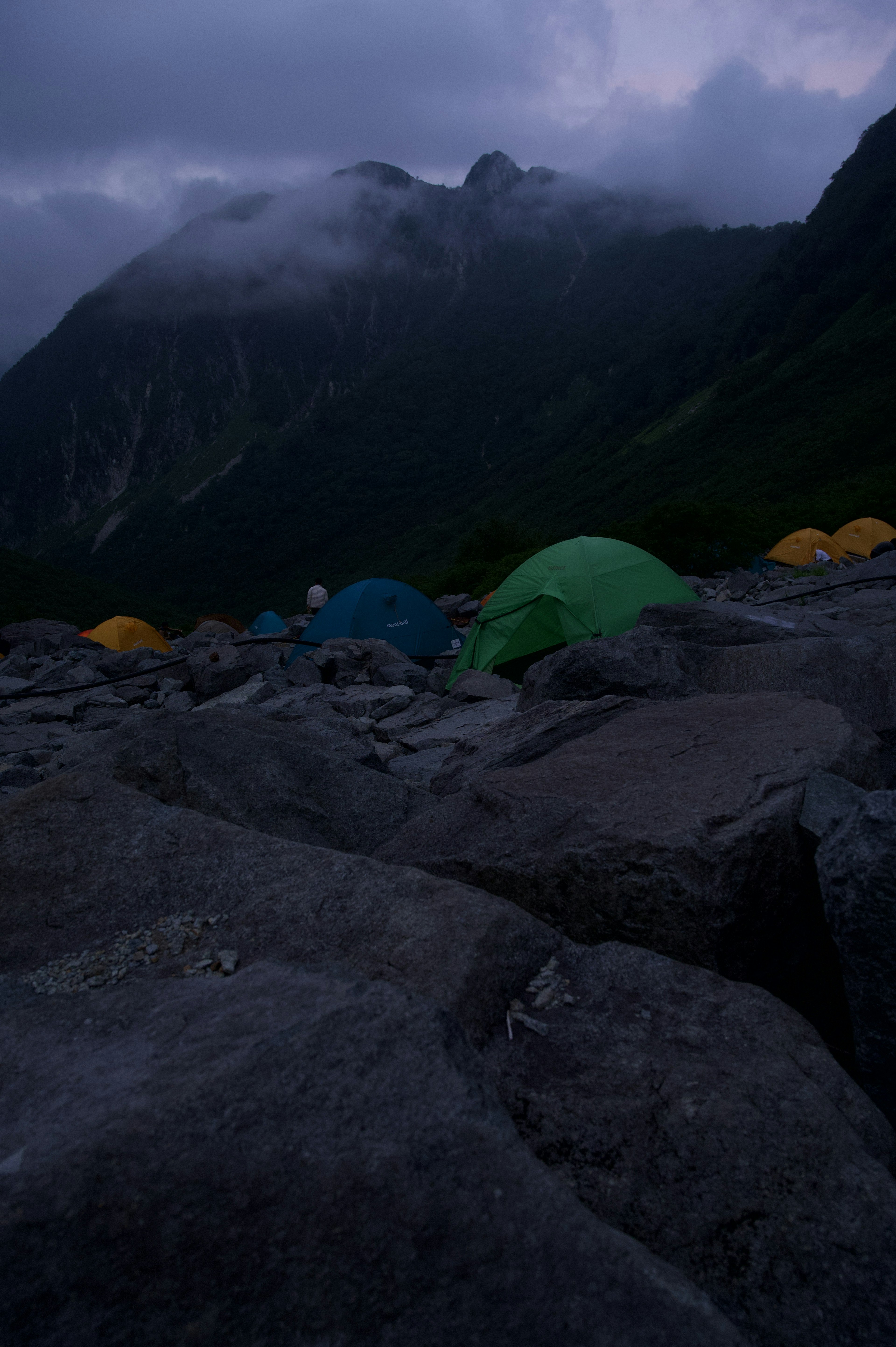 Pemandangan malam dengan tenda hijau dan kuning di latar belakang gunung berkabut