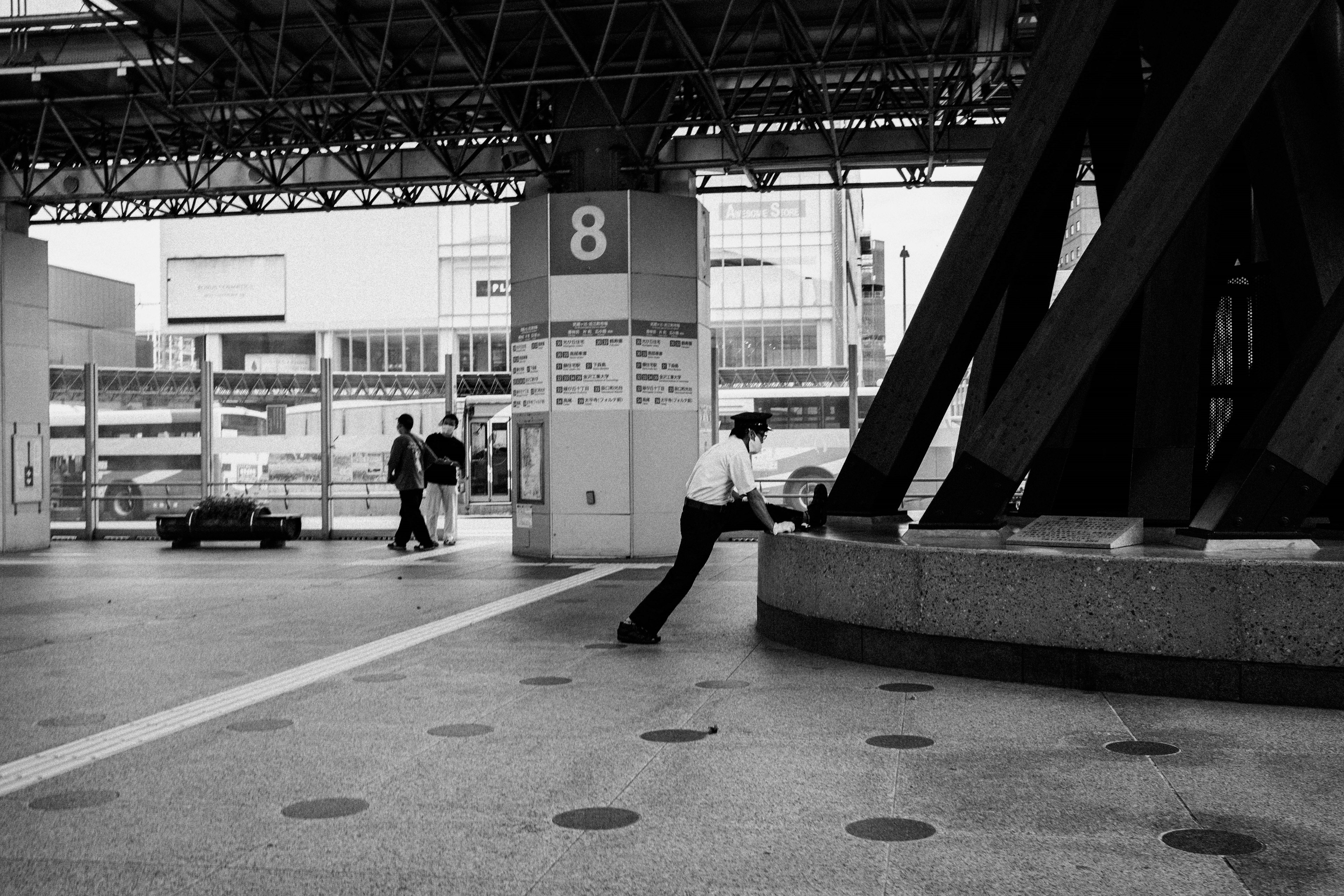 Un hombre apoyado en una columna en una estación de tren en blanco y negro