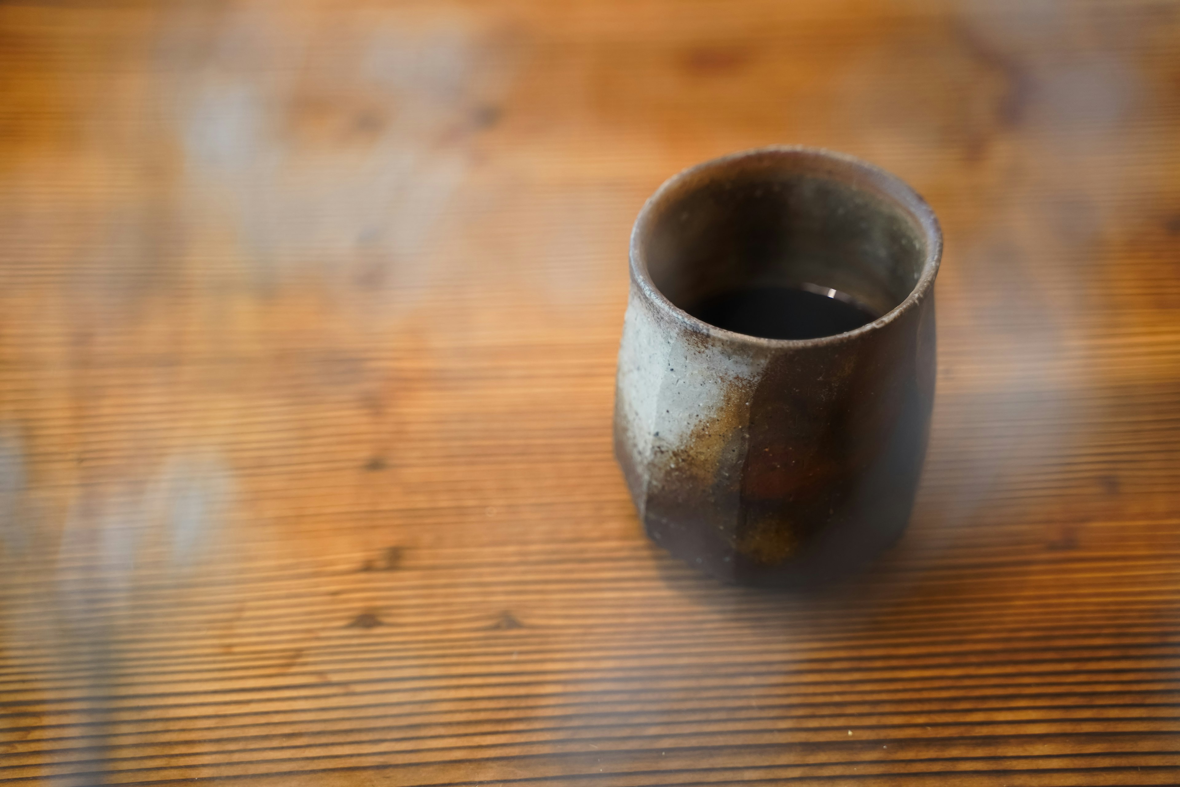 Keramiktasse mit dunkler Flüssigkeit auf einem Holztisch