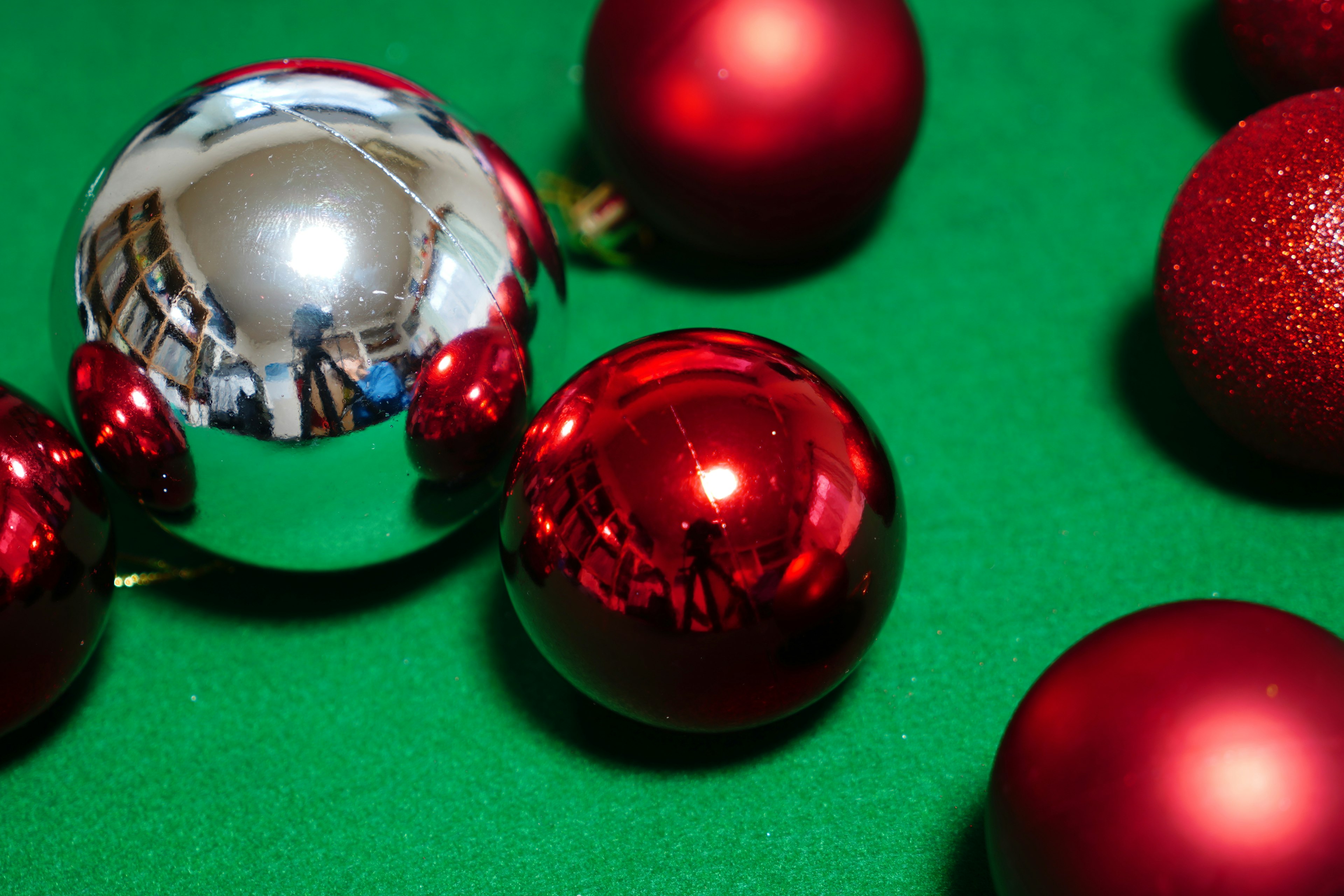 Red Christmas ornaments and a reflective silver ball on green fabric