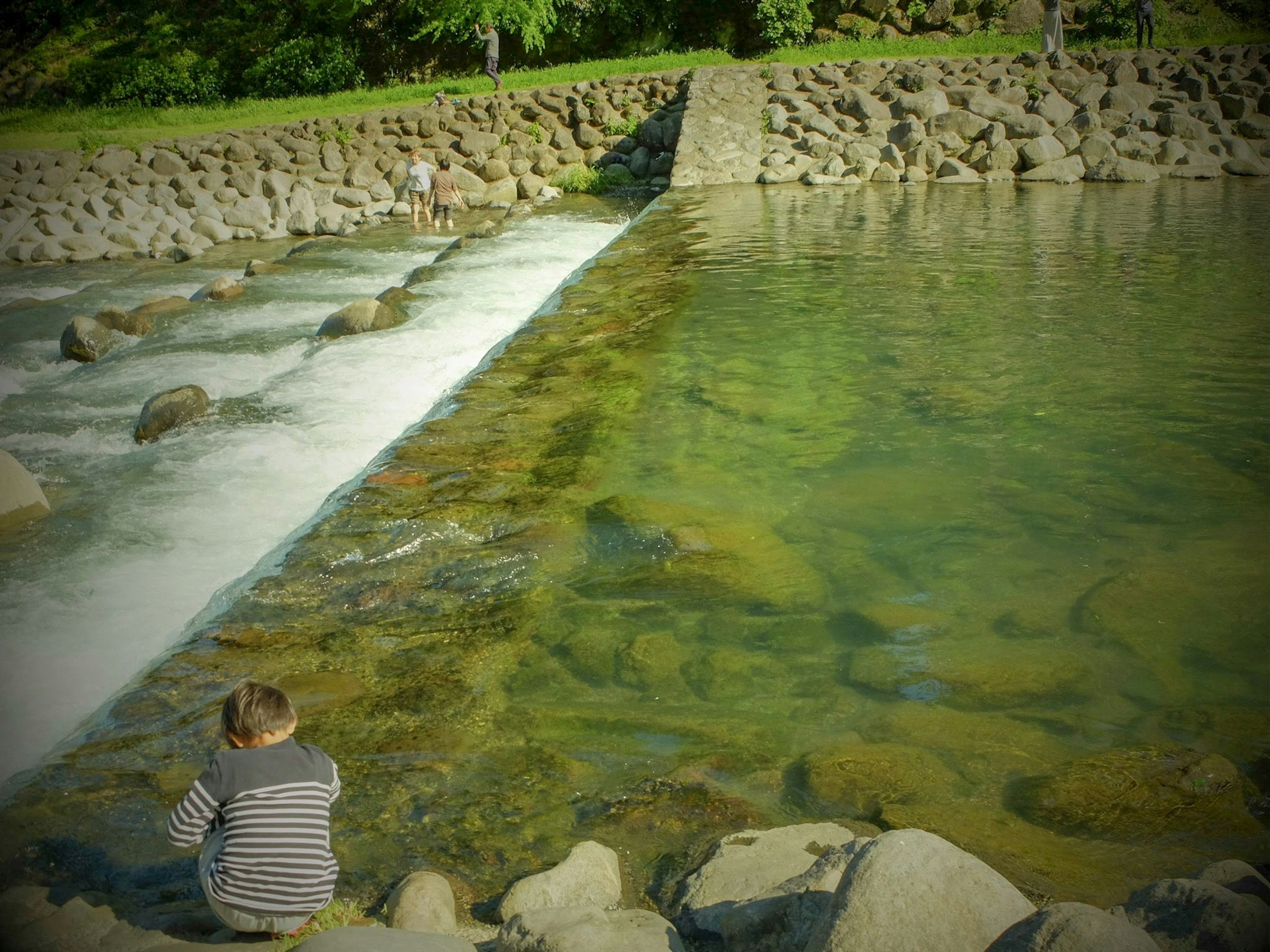 Bambino seduto in riva al fiume con acqua limpida che scorre